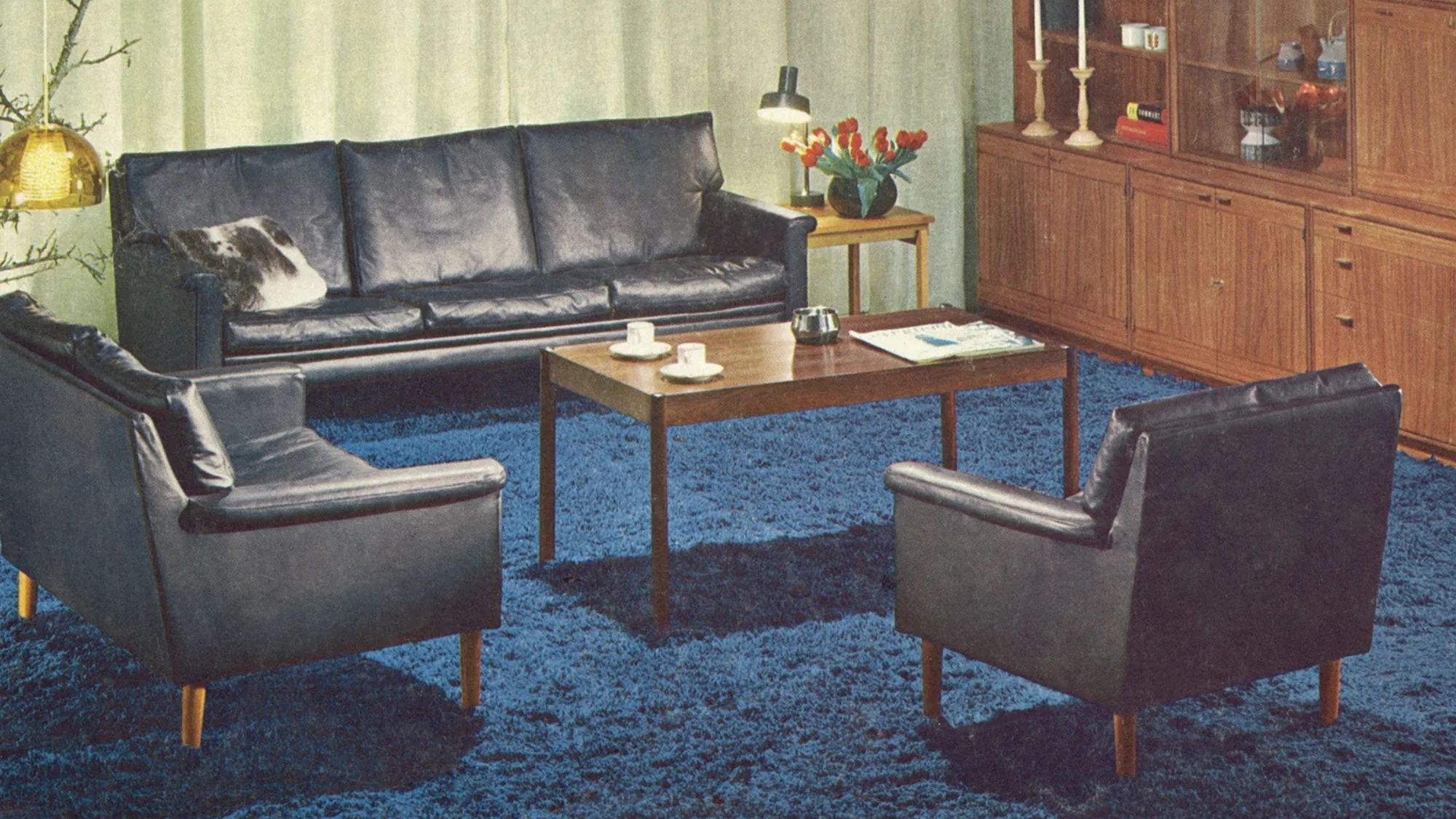 Vintage-IKEA-Wohnzimmer mit blauem Teppich, schwarzen Ledersofas und einer hölzernen Stauraumwand