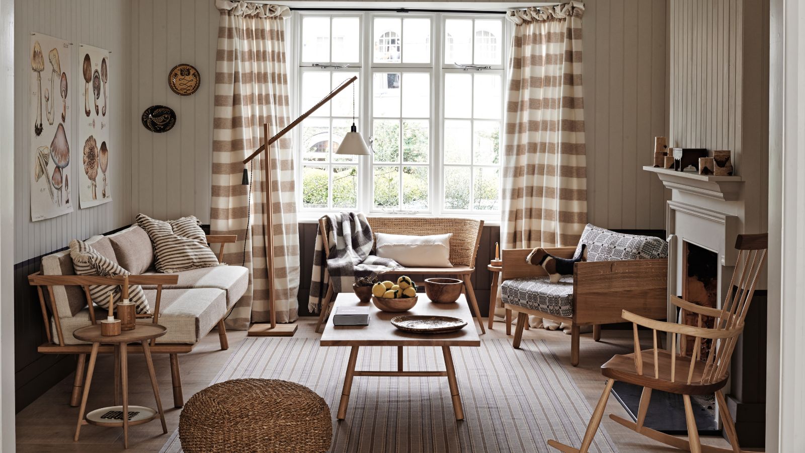 Wohnzimmer im Scandi-Stil mit Gingham-Vorhängen, hölzernen Schaukelstühlen, cremefarbenem Sofa, eckiger Stehlampe und Rattan-Hocker
