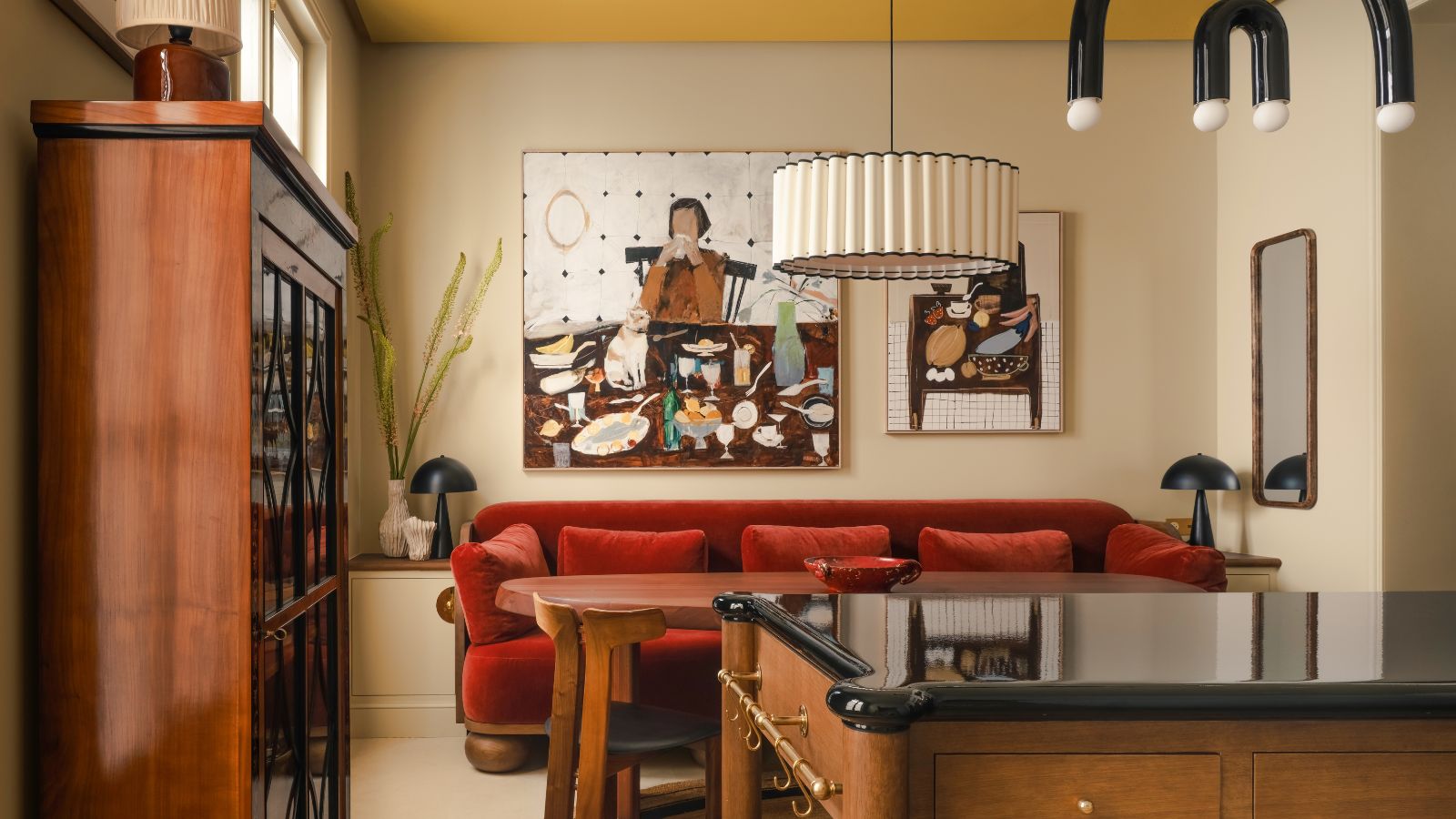 Eine Küche mit warmweißen Wänden, einer Holzinsel und Kommode, einem roten Samtsofa und einer gelben Decke. 