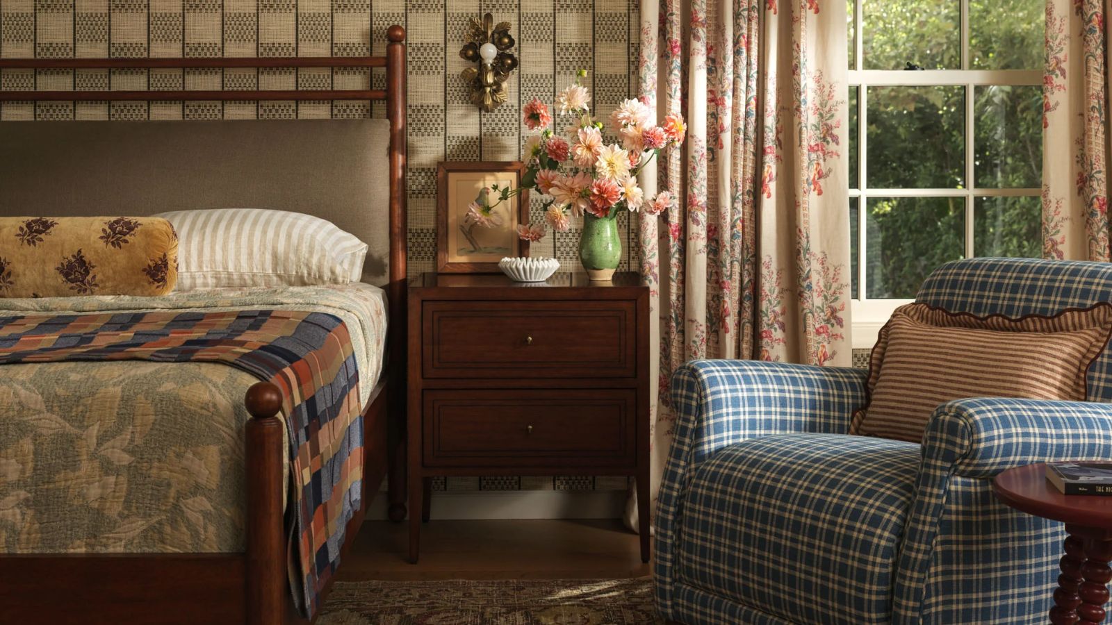 Gemütliches Cottage-Schlafzimmer, entworfen von Heidi Caillier für Lulu und Georgia, mit karierter Tapete, geblümten Vorhängen, kariertem Stuhl sowie Holzbett und Nachttisch