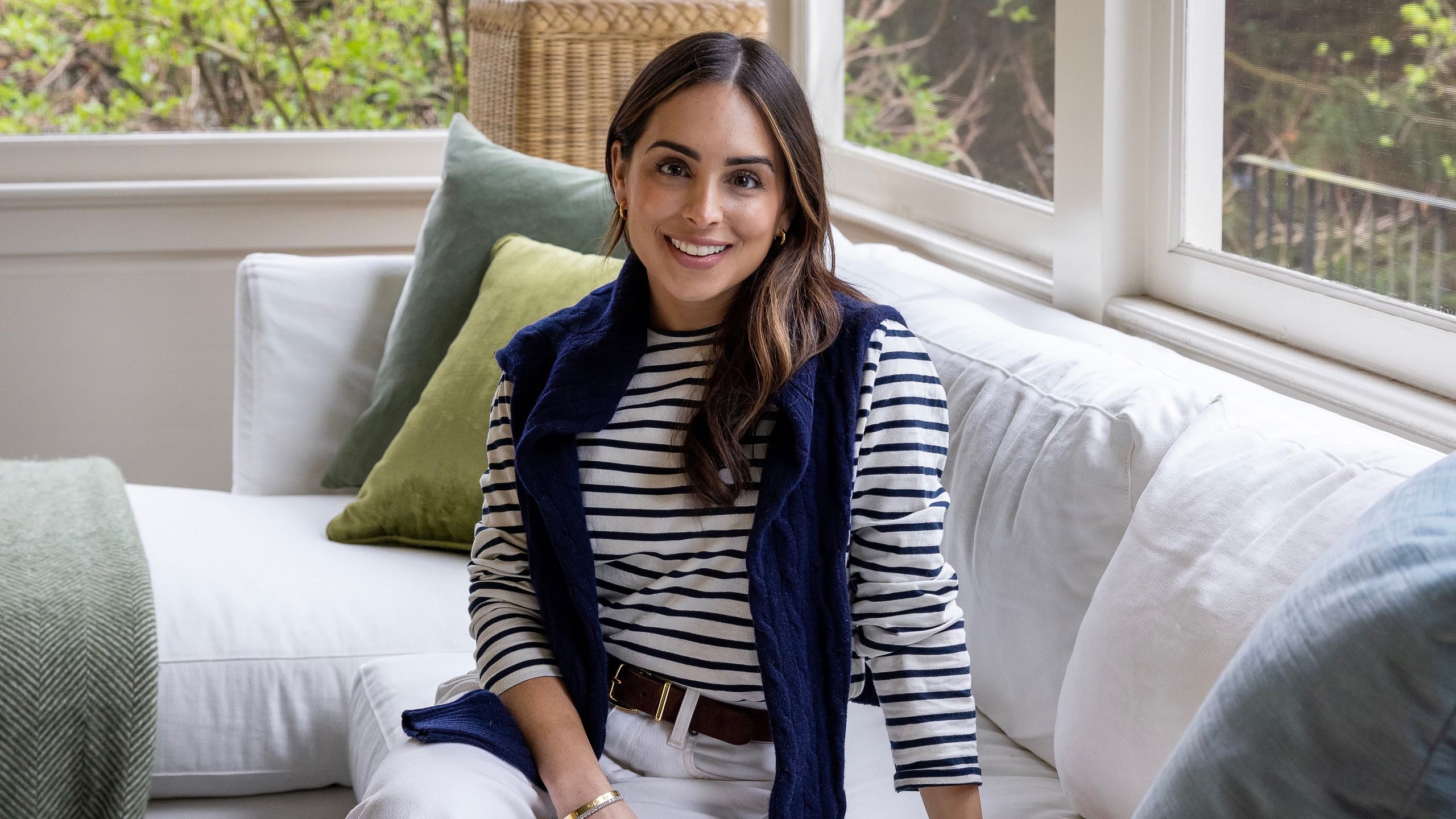 Ariel Okin in a striped top sat on a white sofa looking to camera