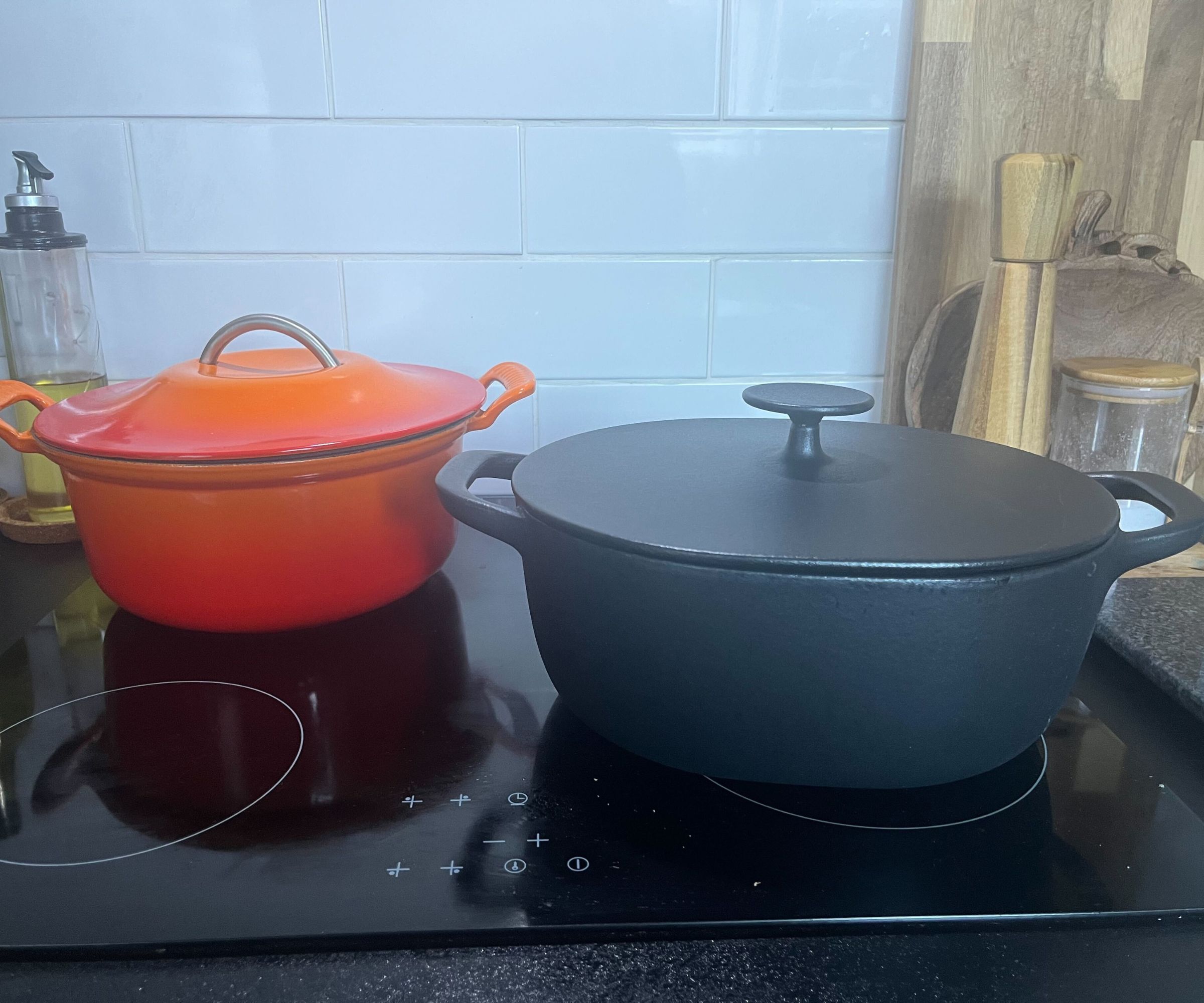 IKEA Schmortopf neben dem Schmortopf von Le Creuset auf einem schwarzen Elektroherd, vor einer weißen Rückwand aus U-Bahnfliesen