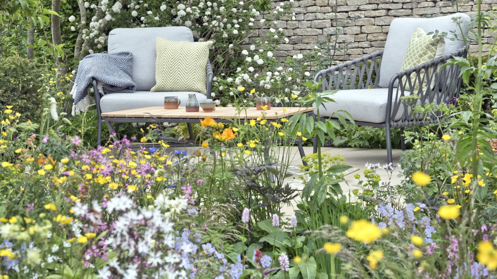 A colourful flower bed in front of a paved seating area in a garden