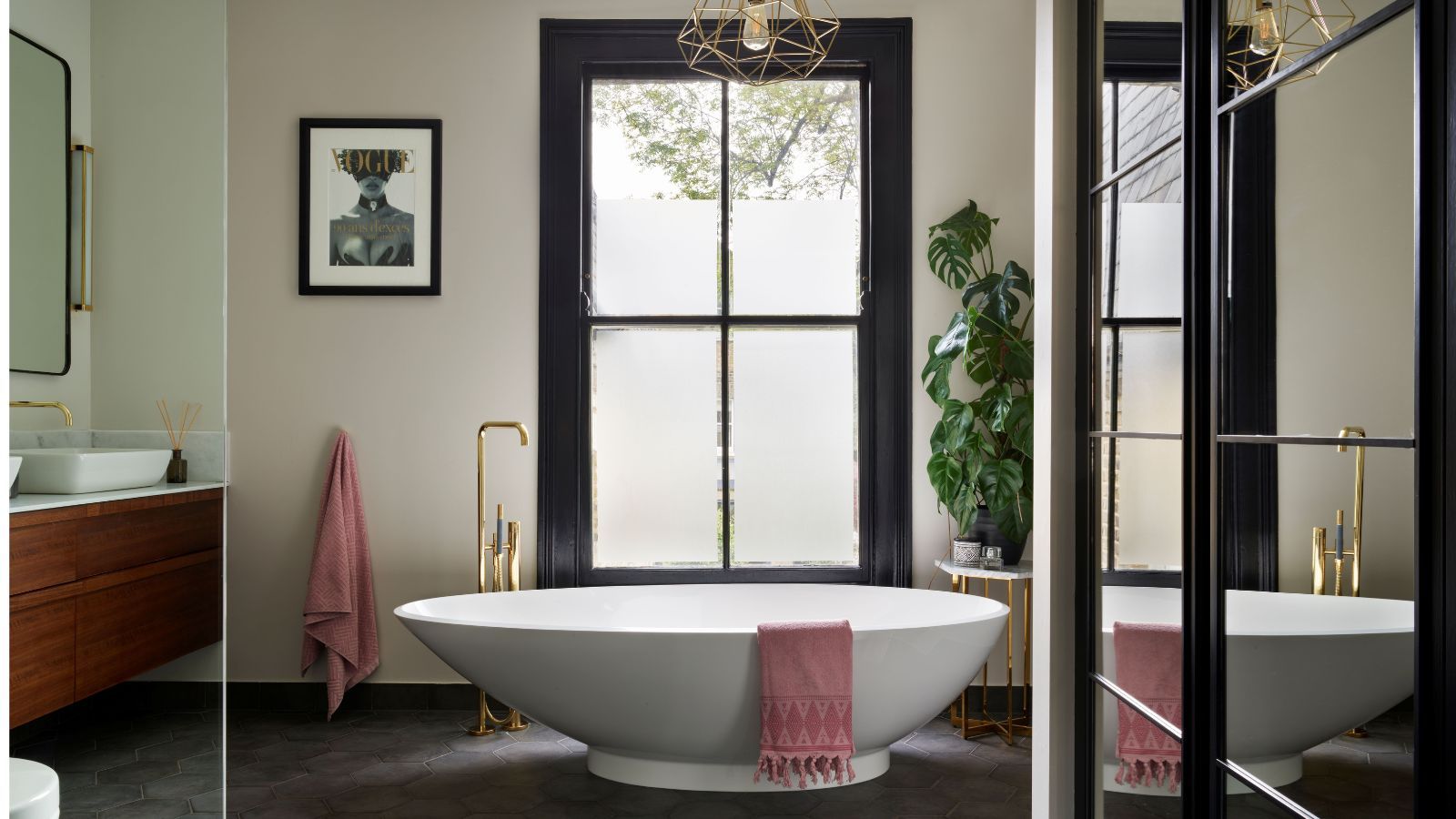 Bright bathroom with freestanding tub and large windows and mirrors, gold hardware and wooden undersink vanity