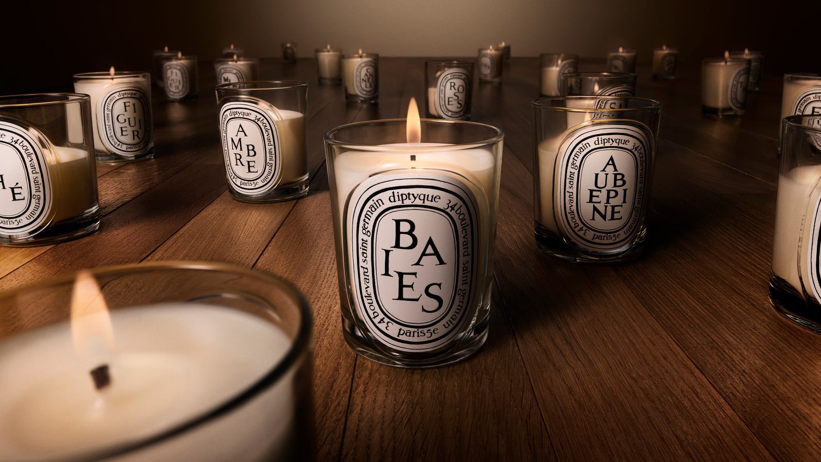 Diptyque relaunch candles in glass vessels with white labels and black text, pictured on a wooden surface