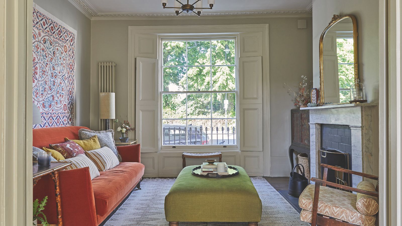 Wohnzimmer mit Erkerfenster, Marmorkamin, orangefarbenem Sofa, Wandteppich und grünem Ottoman