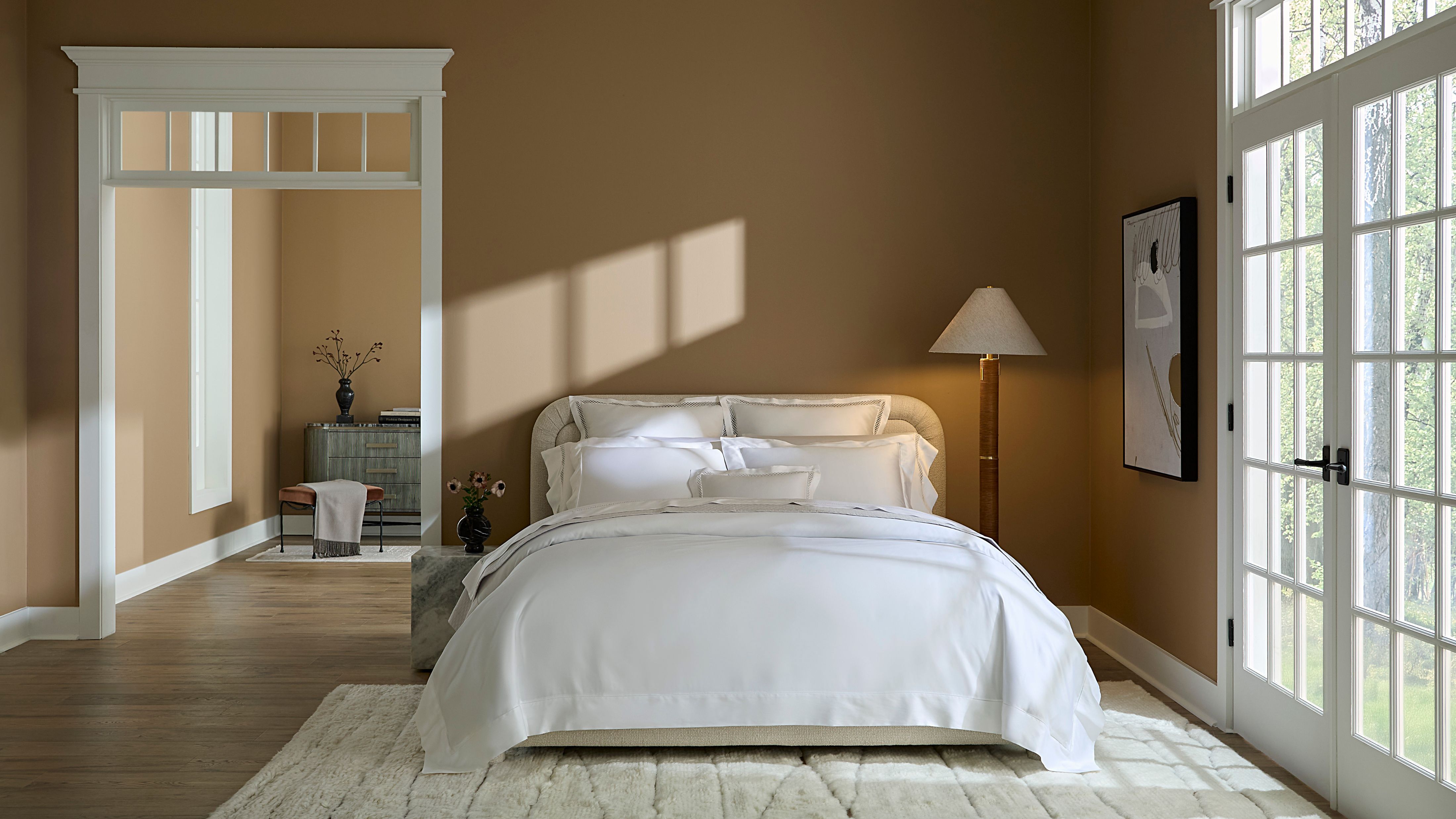 Weiße Satinbettwäsche Sferra Gize 45, abgebildet in einem neutralen, sonnendurchfluteten Schlafzimmer neben zeitgenössischer Kunst und einer übergroßen Stehlampe