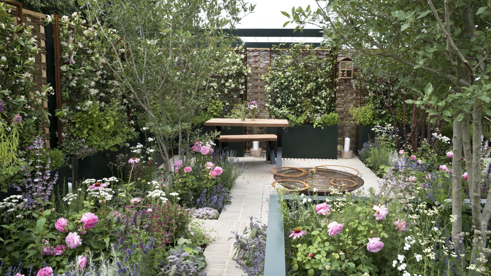 A modern garden with raised beds, seating area, and beds filled with flowers and shrubs