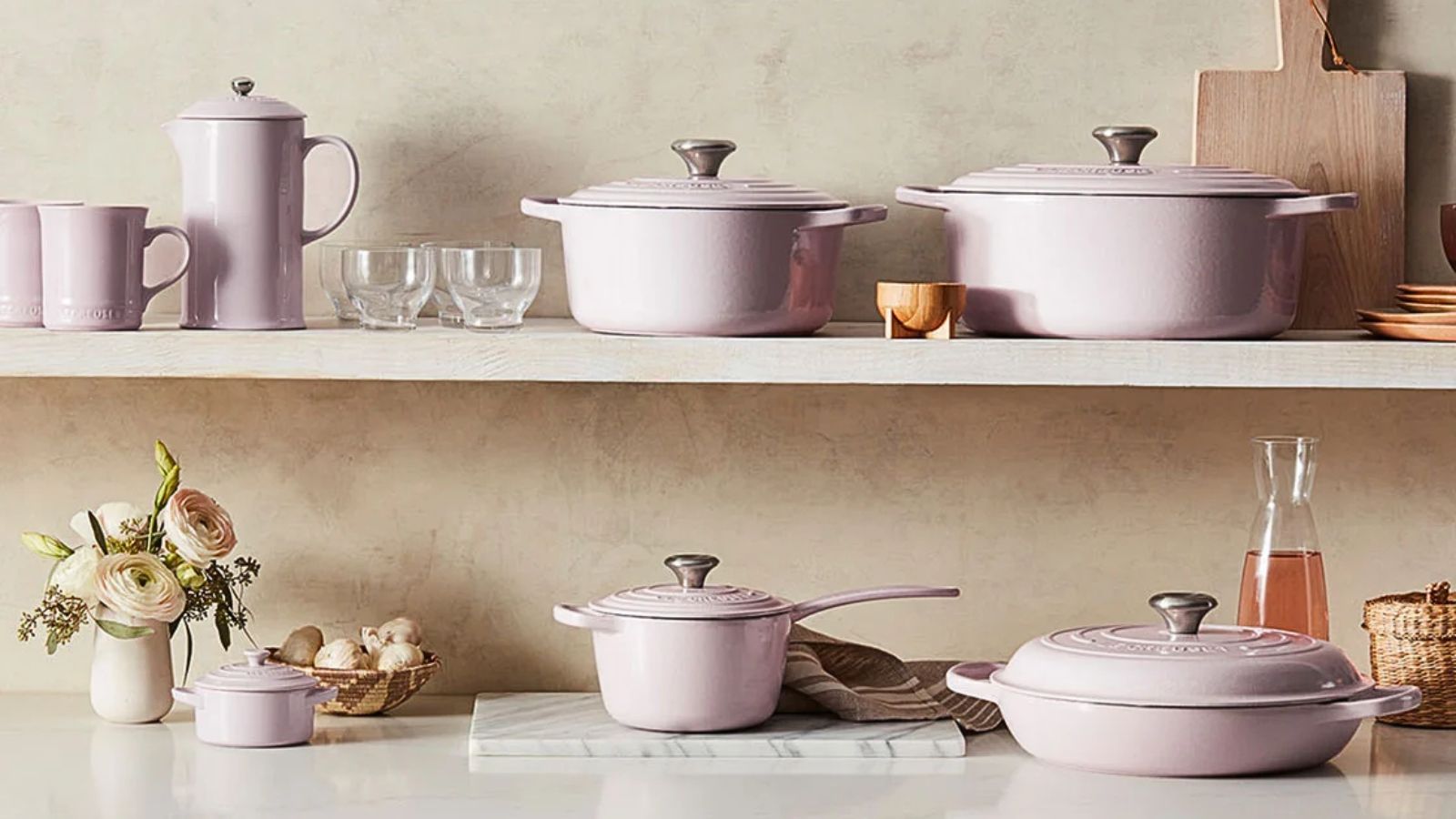 Das komplette Le Creuset Schalotten-Set bestehend aus Pfannen und Deckeln auf einer Arbeitsplatte und einem Regal. 