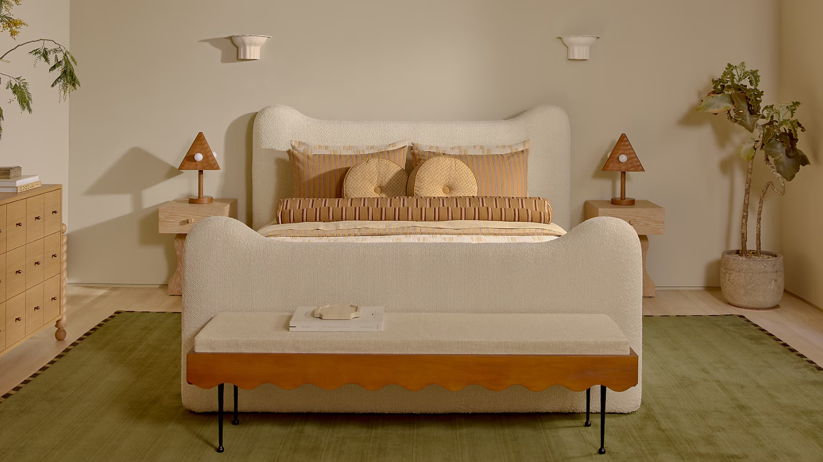 ein warmes, skurriles Schlafzimmer mit einem grünen Teppich, einem weißen Polsterbett, einer Bank am Fußende des Bettes und Kissen auf dem Bett