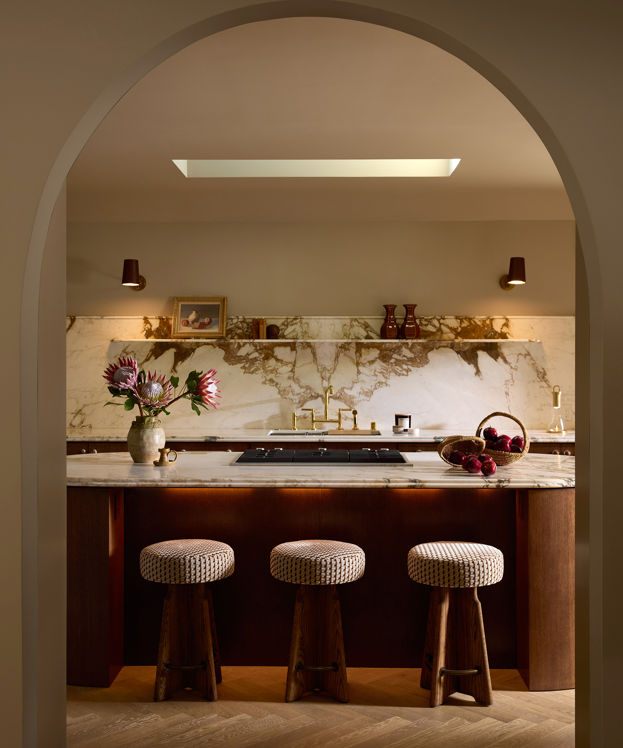 eine Küche, gesehen durch eine gewölbte Tür mit drei modernen Hockern vor einer Holzinsel