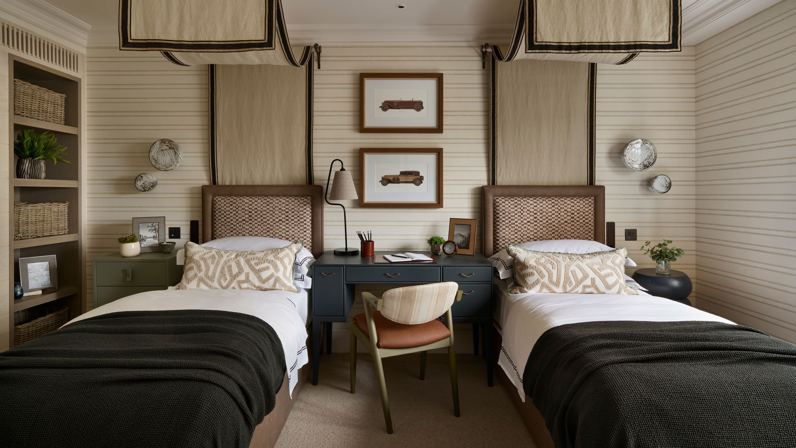 ein Kinderzimmer mit zwei Einzelbetten, beige gestreiften Wänden und zwei Himmelbetten, einem Schreibtisch in der Mitte, einem Bücherregal und dunkelgrün-blauen Farbakzenten