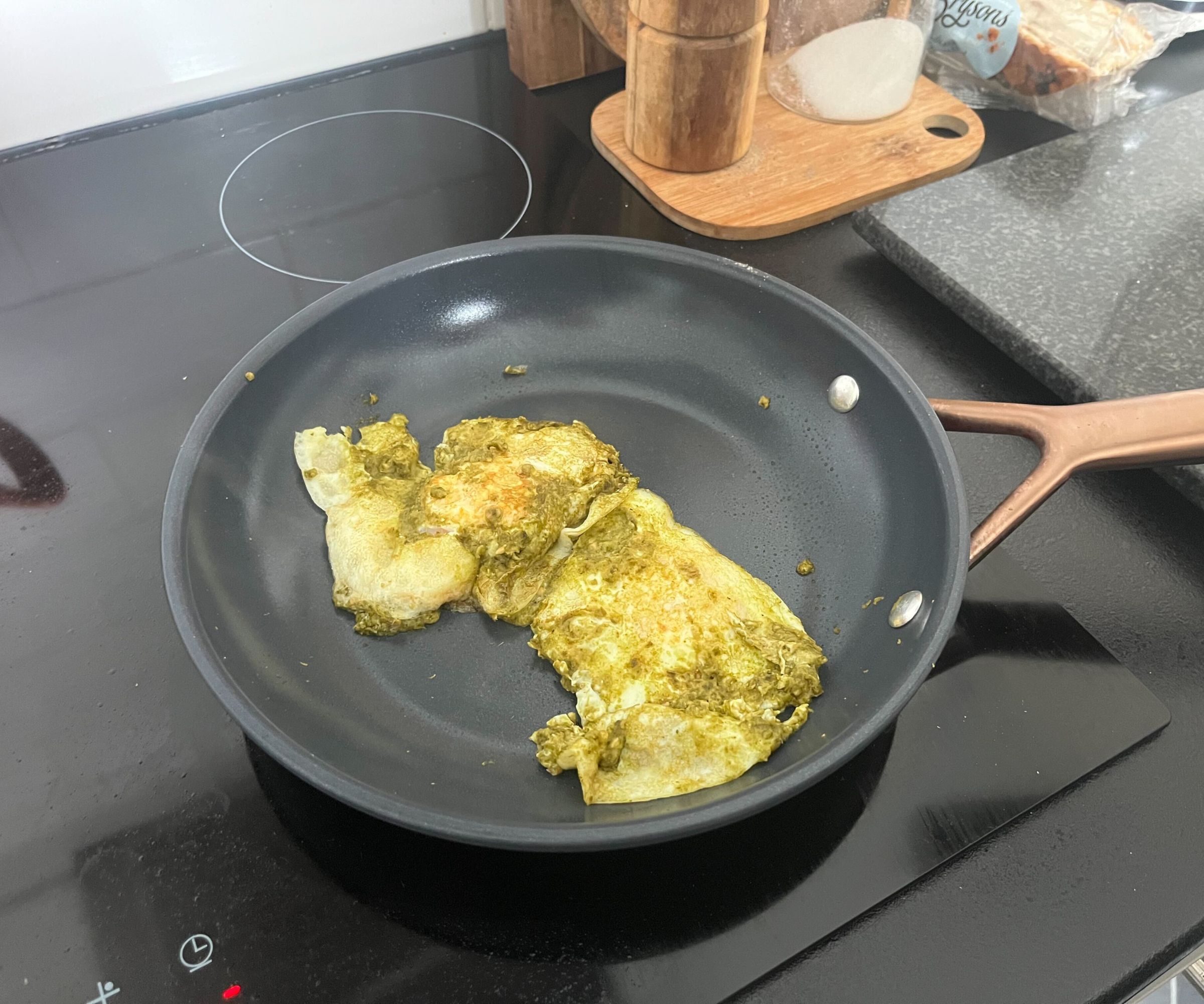 Spiegeleier und grünes Pesto in einer kleinen blauen Keramikpfanne.