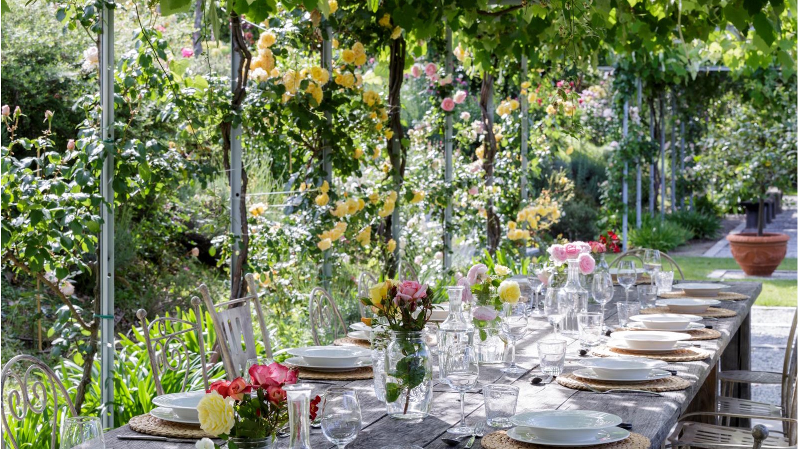 Esstisch im Freien unter Weinreben. Mit Blumen dekorierter Tisch