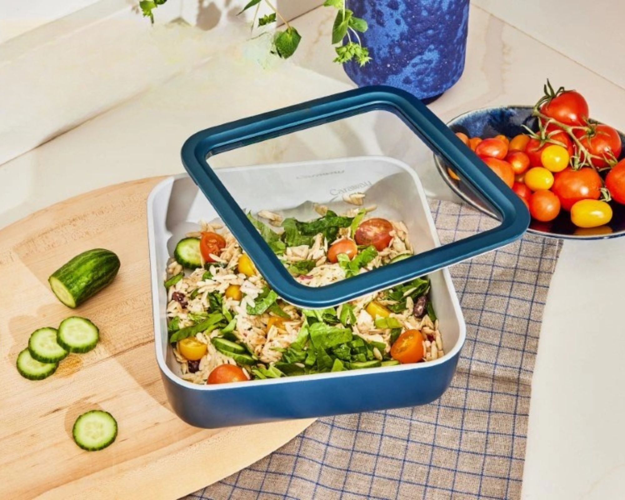 Marineblaue Kümmel-Lebensmittelaufbewahrung auf einem Tisch mit einem Teller Tomaten daneben