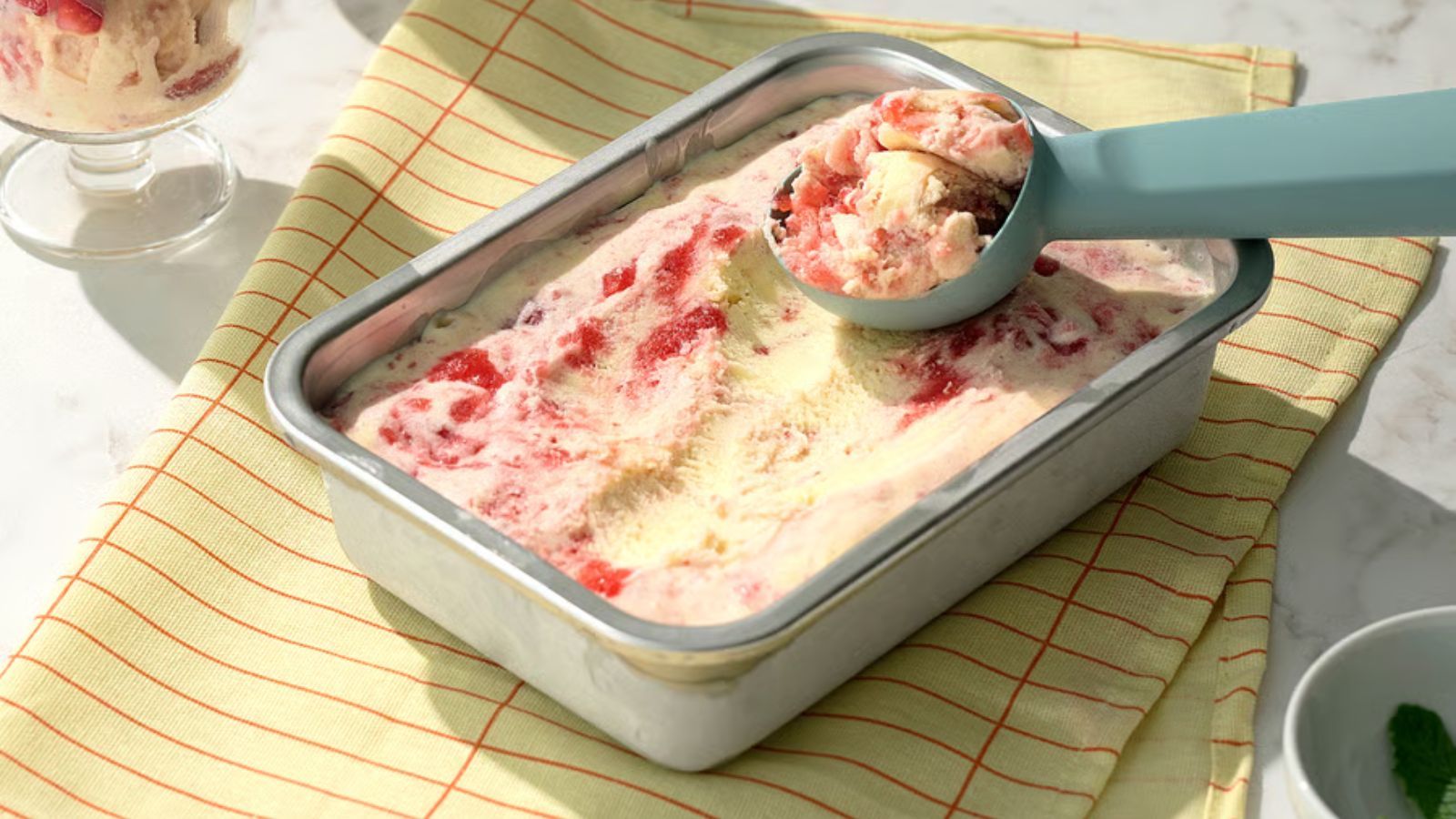 A small rectangular stainless steel food container filled with ice cream with a scoop on top