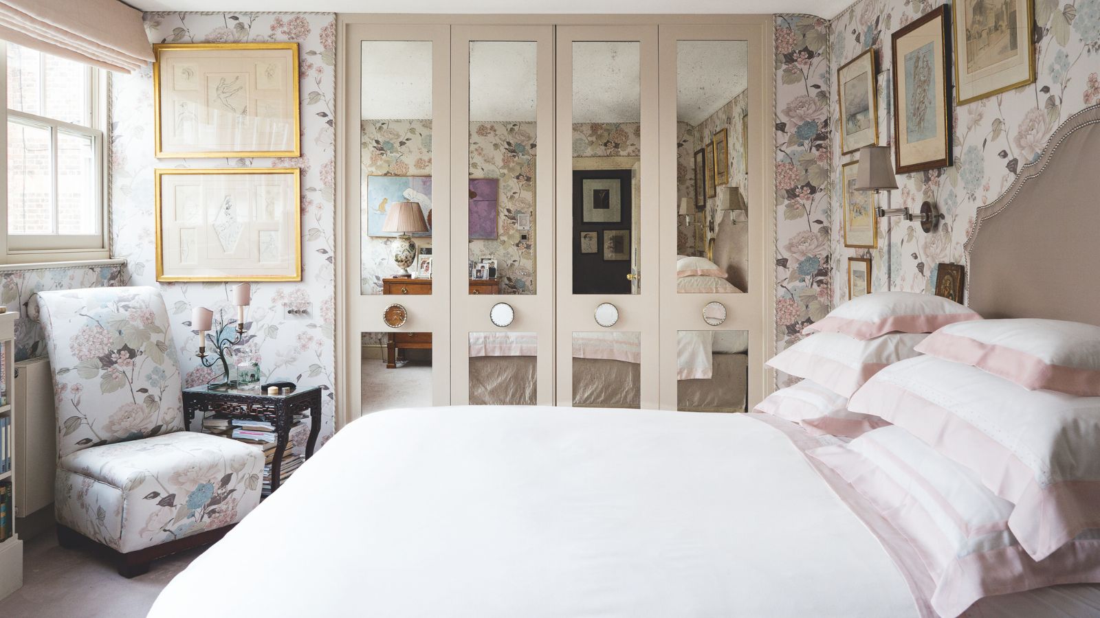 Kleines Schlafzimmer mit verspiegeltem viertürigem Einbauschrank, weißer Bettwäsche, kleinem Stuhl mit Beistelltisch und floraler Pastelltapete