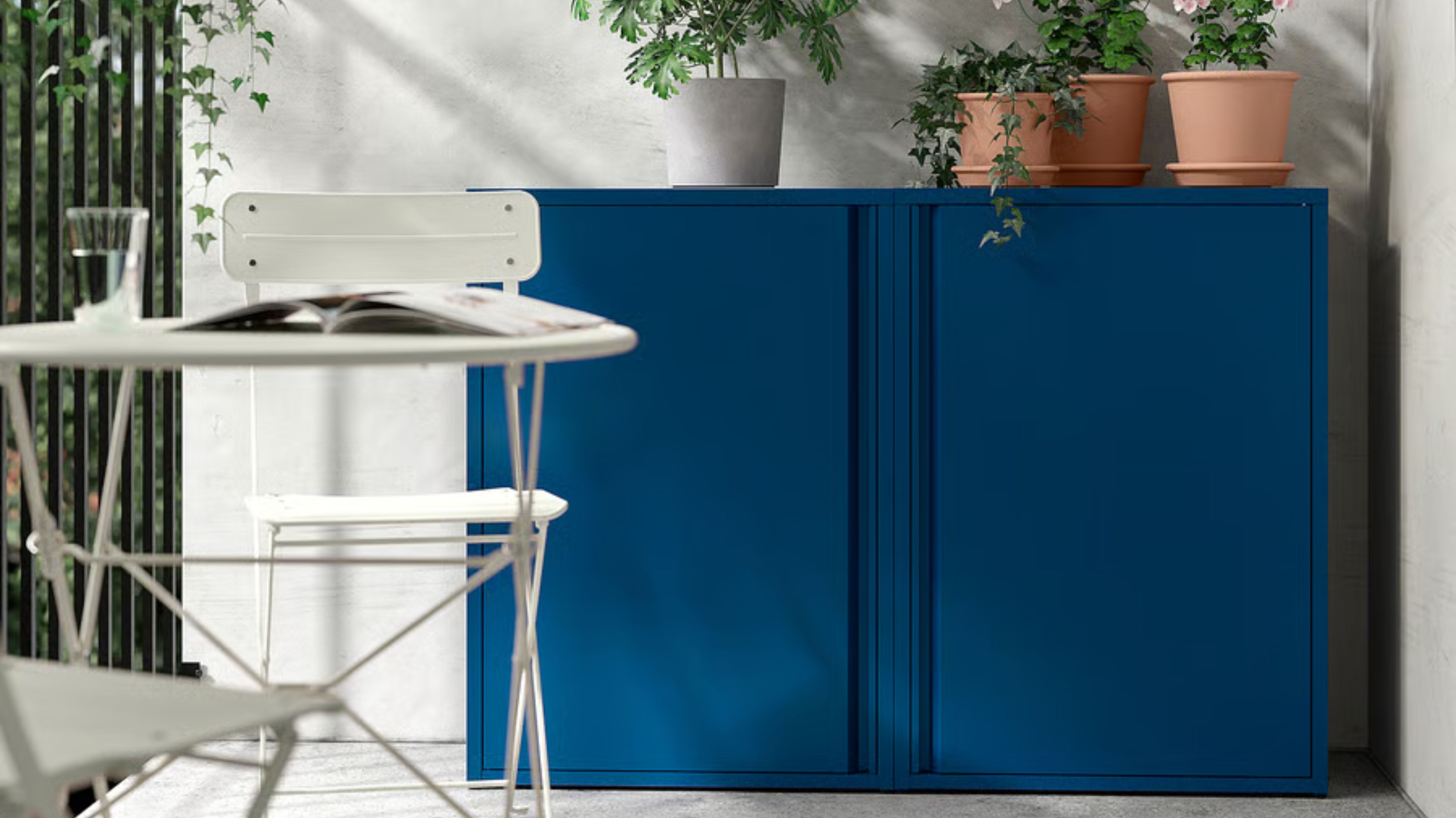 Zwei IKEA SUNDSÖ-Außenschränke in Kobalt mit Topfpflanzen, versteckt in der Ecke eines strahlend weißen Terrassenbereichs 