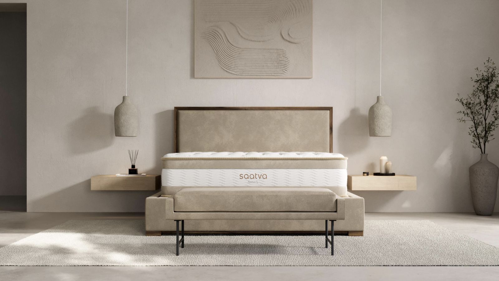 A Saatva Rx mattress in a minimalist cream bedroom on a beige bedframe, with a white rug underneath, and two wooden bedside tables. Above the bed is a large gray artwork and two hanging lamps