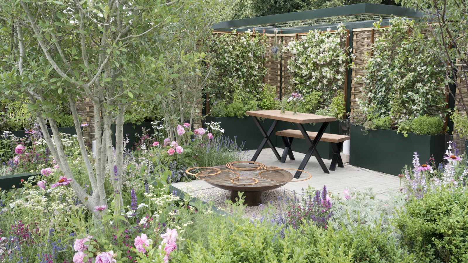 Ein moderner Garten mit Hochbeeten, Spalieren und einer möblierten Terrasse