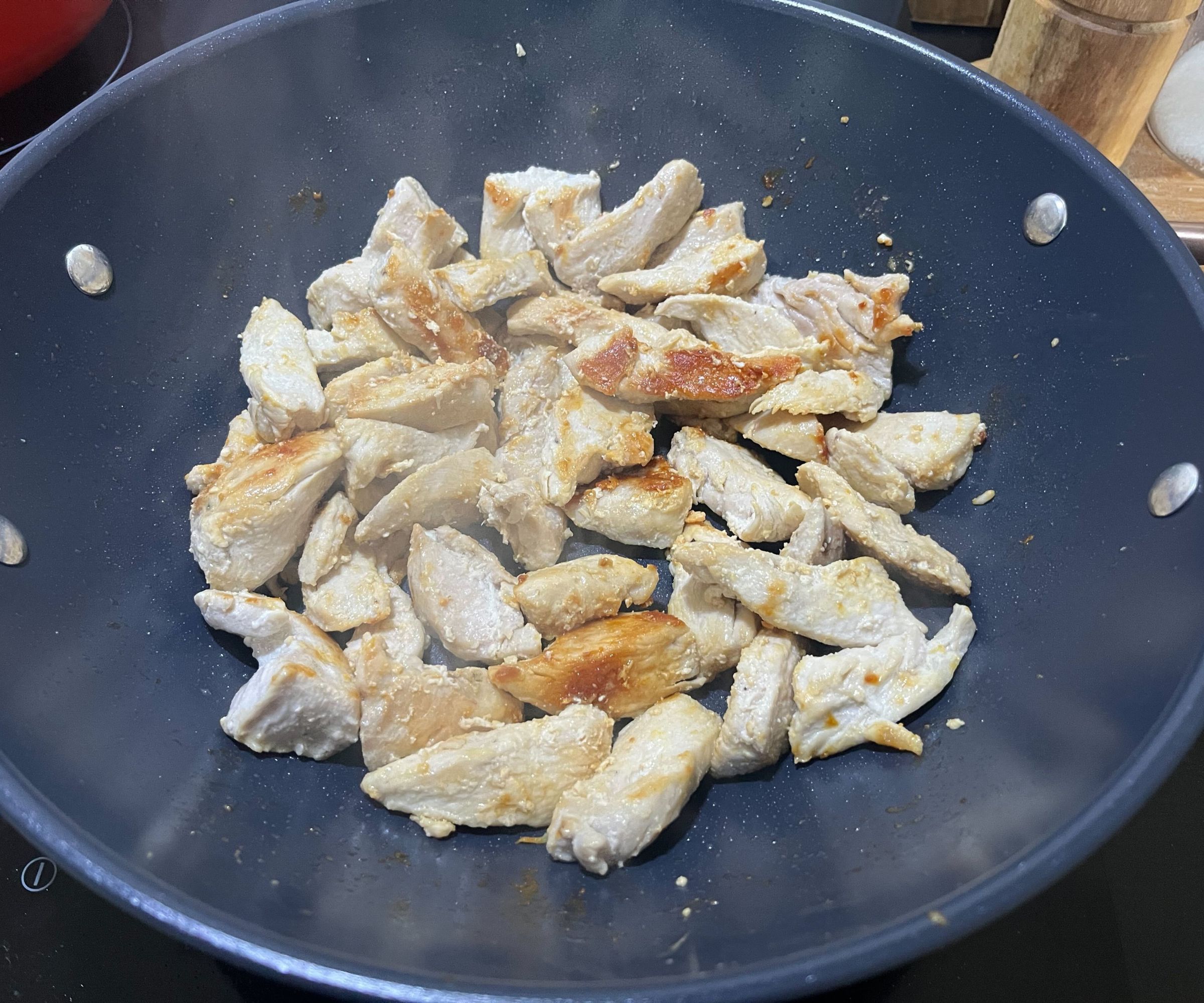 Hähnchen in einem blauen Keramik-Wok bräunen