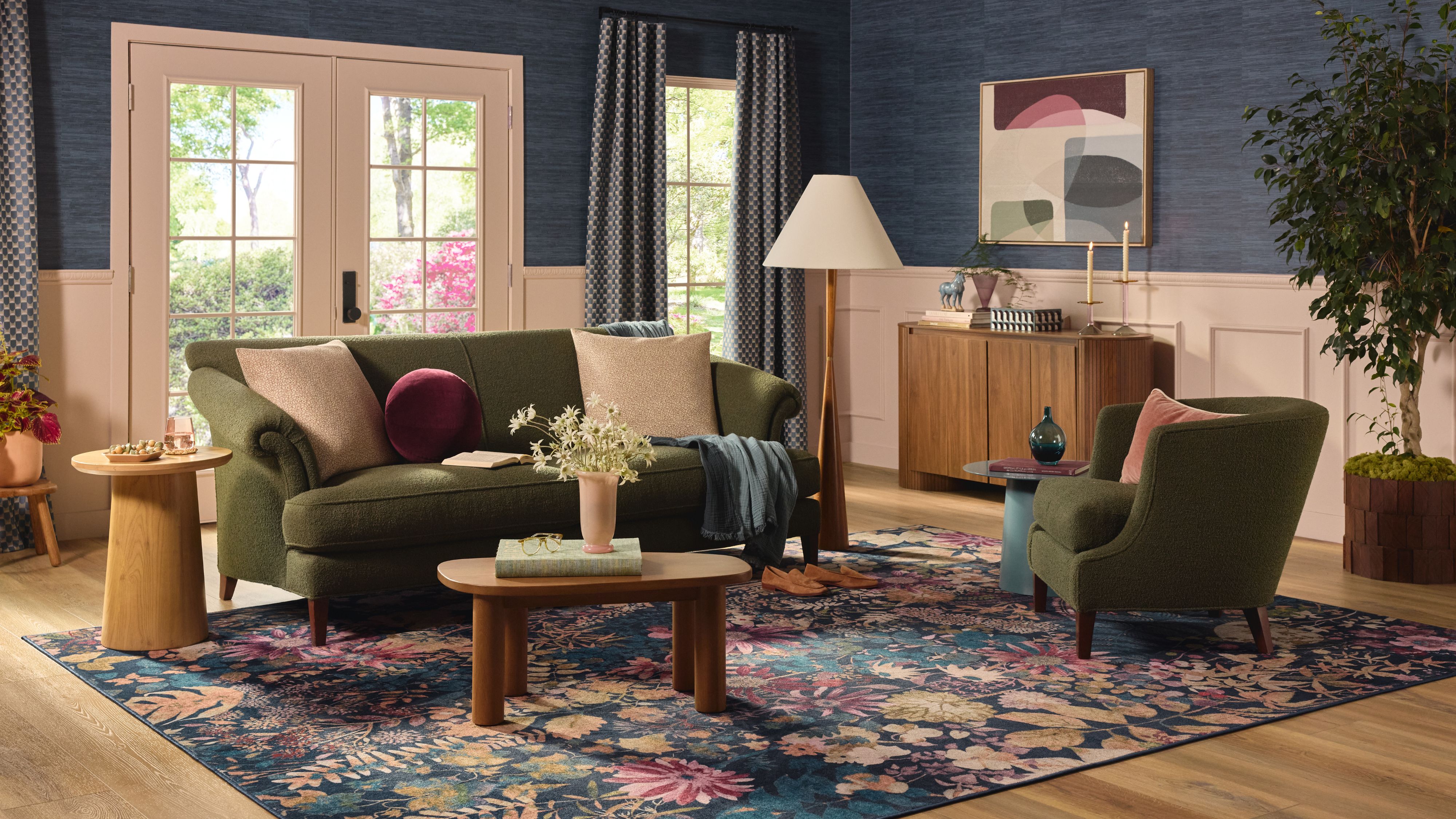 In Juwelentönen gehaltenes Wohnzimmer mit Sitzmöbeln in sattem Grün, einem Couchtisch aus Holz und einem floralen, großformatigen Blumenteppich