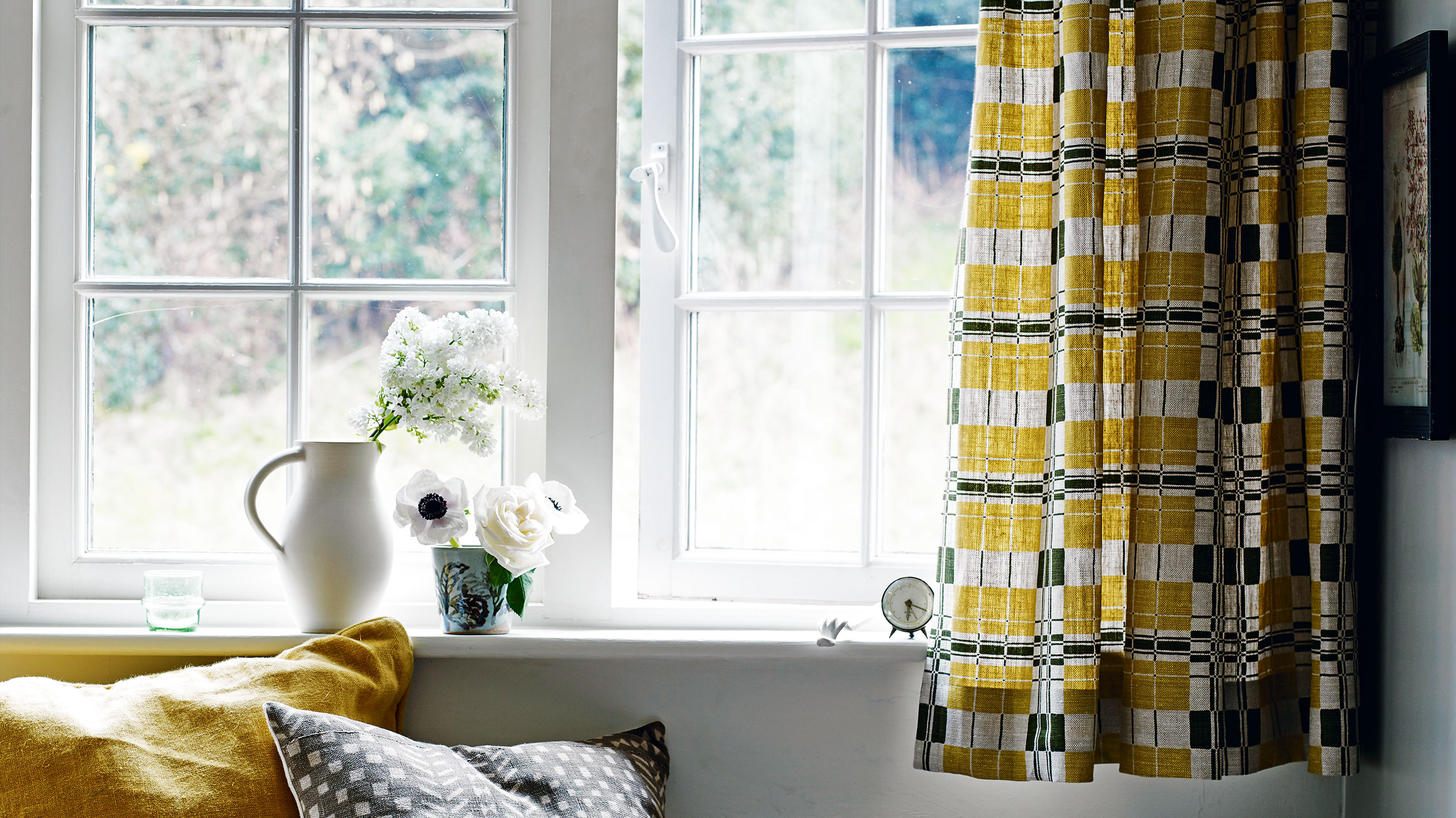 Offenes Fenster und gelber Vorhang mit Fenstersitz und Blumen