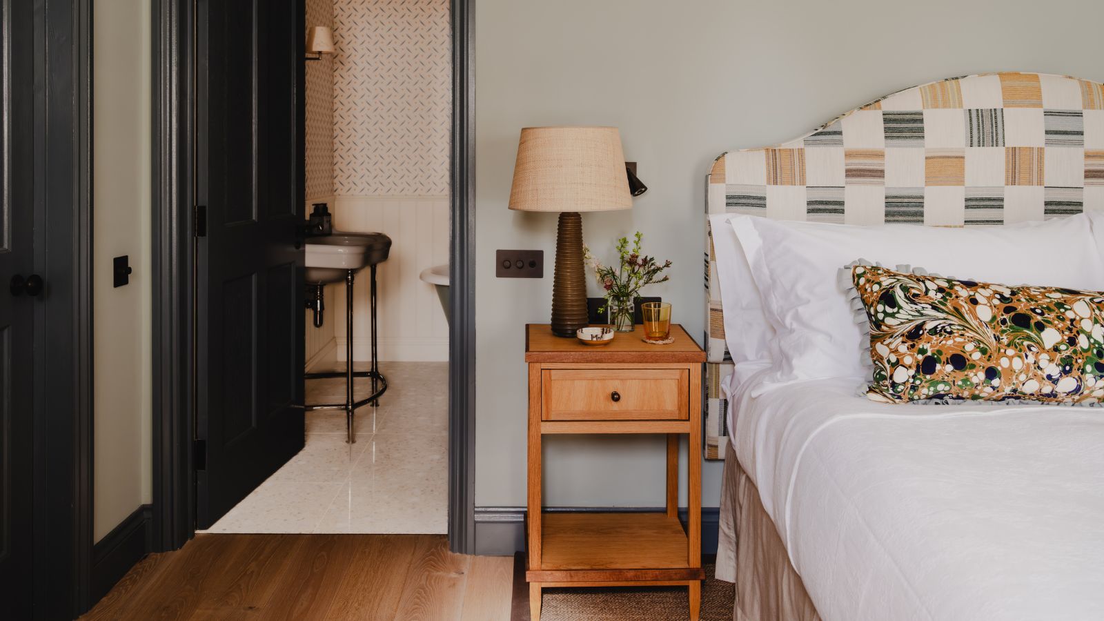 ein blass hellblaues Schlafzimmer mit dunkelblau gestrichenen Zierleisten und Türen mit einem Patchwork-gelben Kopfteil, einem Nachttisch aus Holz und einem Kissen mit Marmordruck