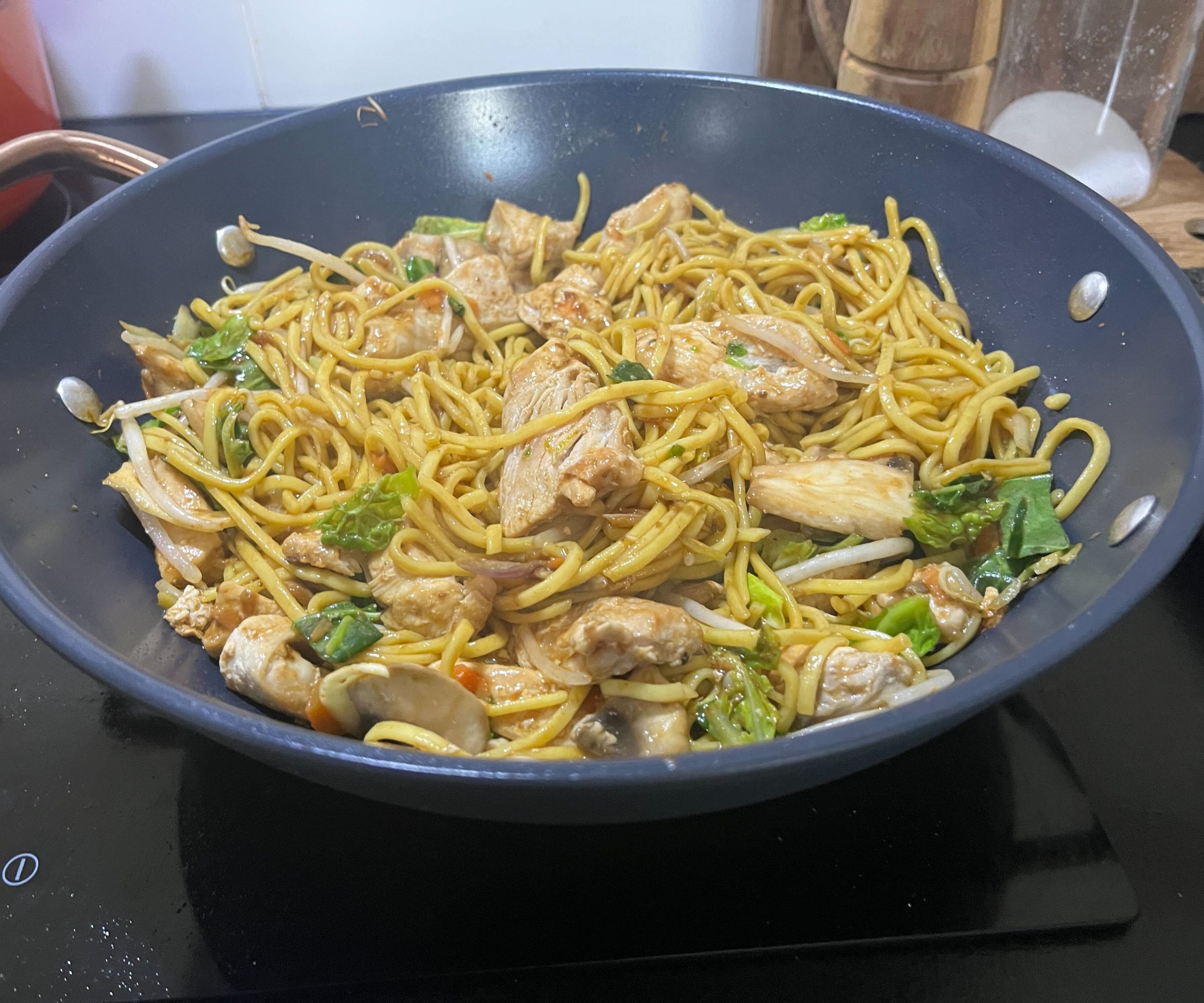 Ein gebratenes Hähnchen mit Eiernudeln in einem blauen Keramik-Wok.