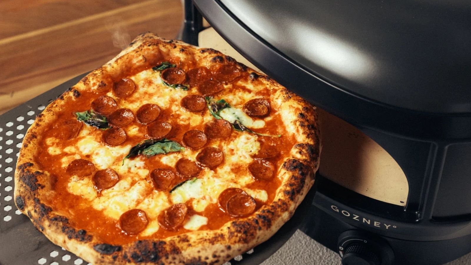 Eine gekochte Peperoni-Pizza, die auf einem perforierten Pizzastück aus einem schwarzen Slimline-Pizzaofen kommt. 