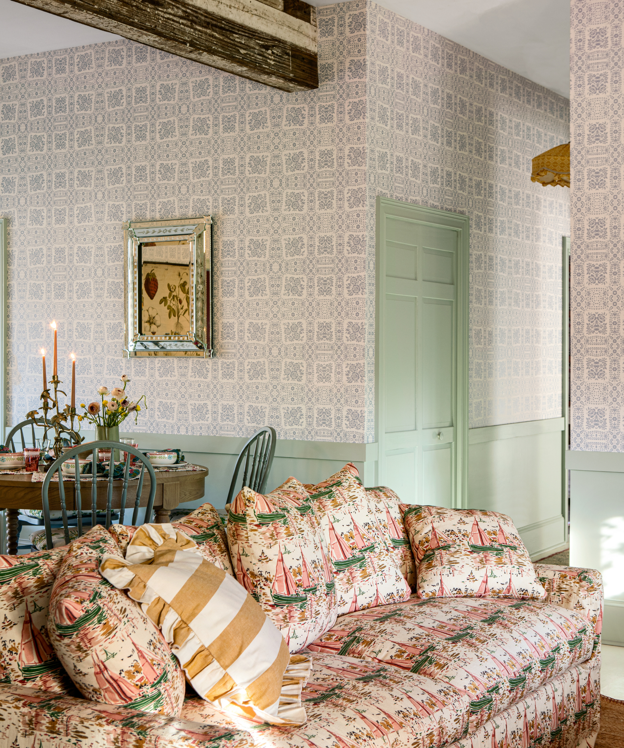 ein Wohnzimmer mit einer großen bedruckten Couch, einem kleinen Esstisch dahinter, blau bedruckter Tapete und mintgrüner Farbe 