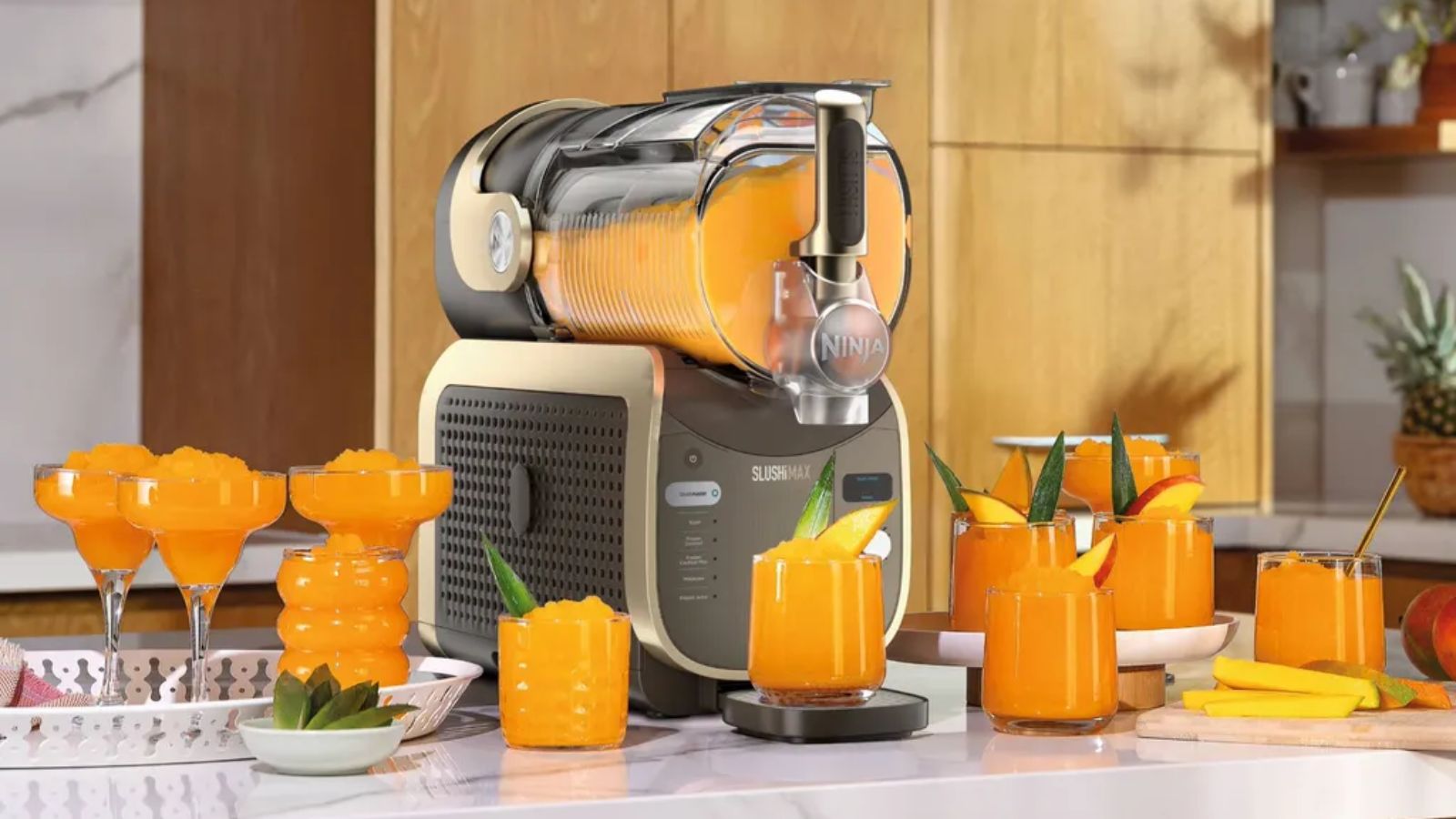 Die schwarz-goldene Ninja-Slushi-Max-Maschine, gefüllt mit Orangenmatsch, umgeben von mehreren Gläsern Orangenmatsch auf einer Marmortheke. 