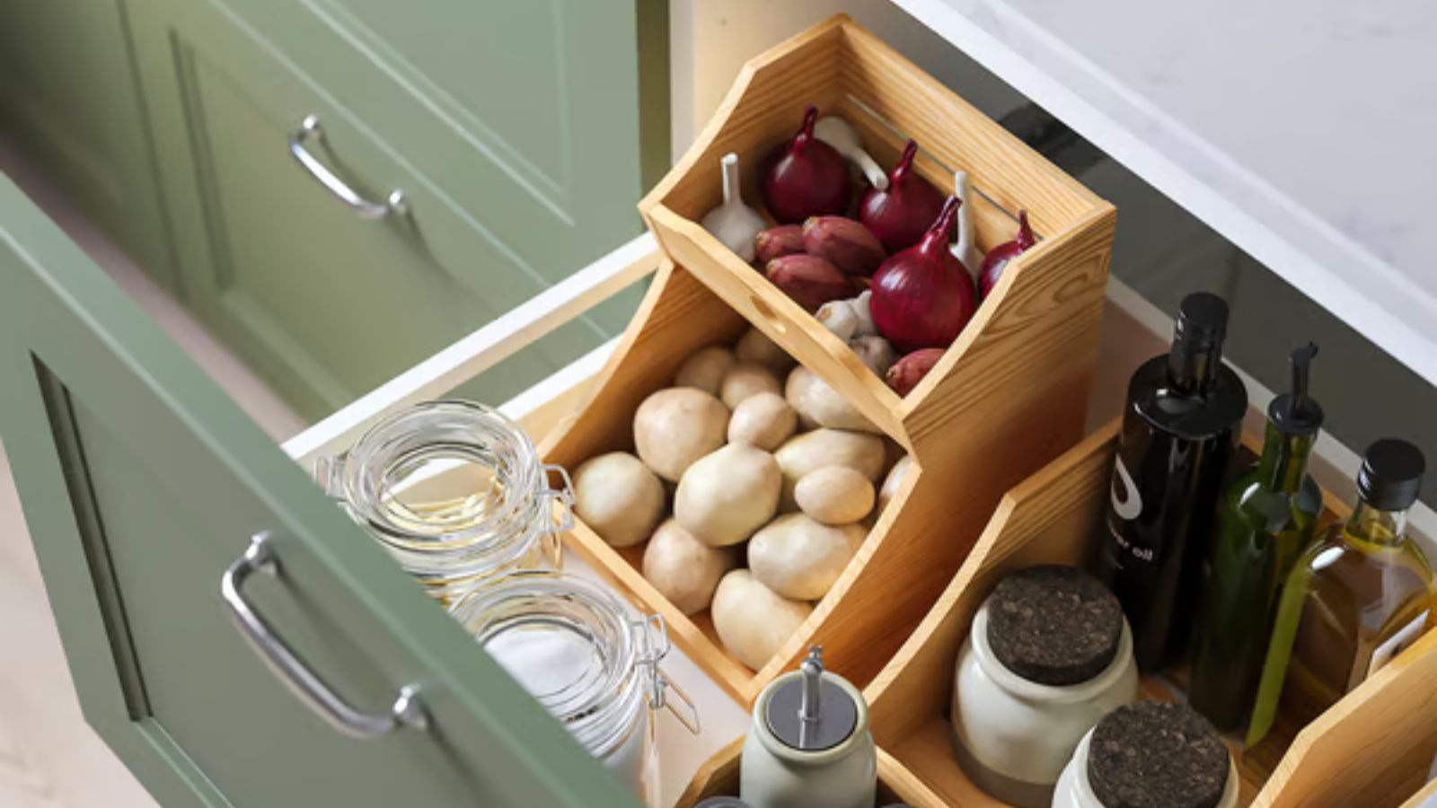 Heldenfoto der gestapelten hölzernen Lebensmittelorganisatoren von IKEA in einer tiefen, offenen Küchenschublade. Es ist oben mit Zwiebeln und Knoblauch gefüllt und in der unteren Ebene mit Kartoffeln.