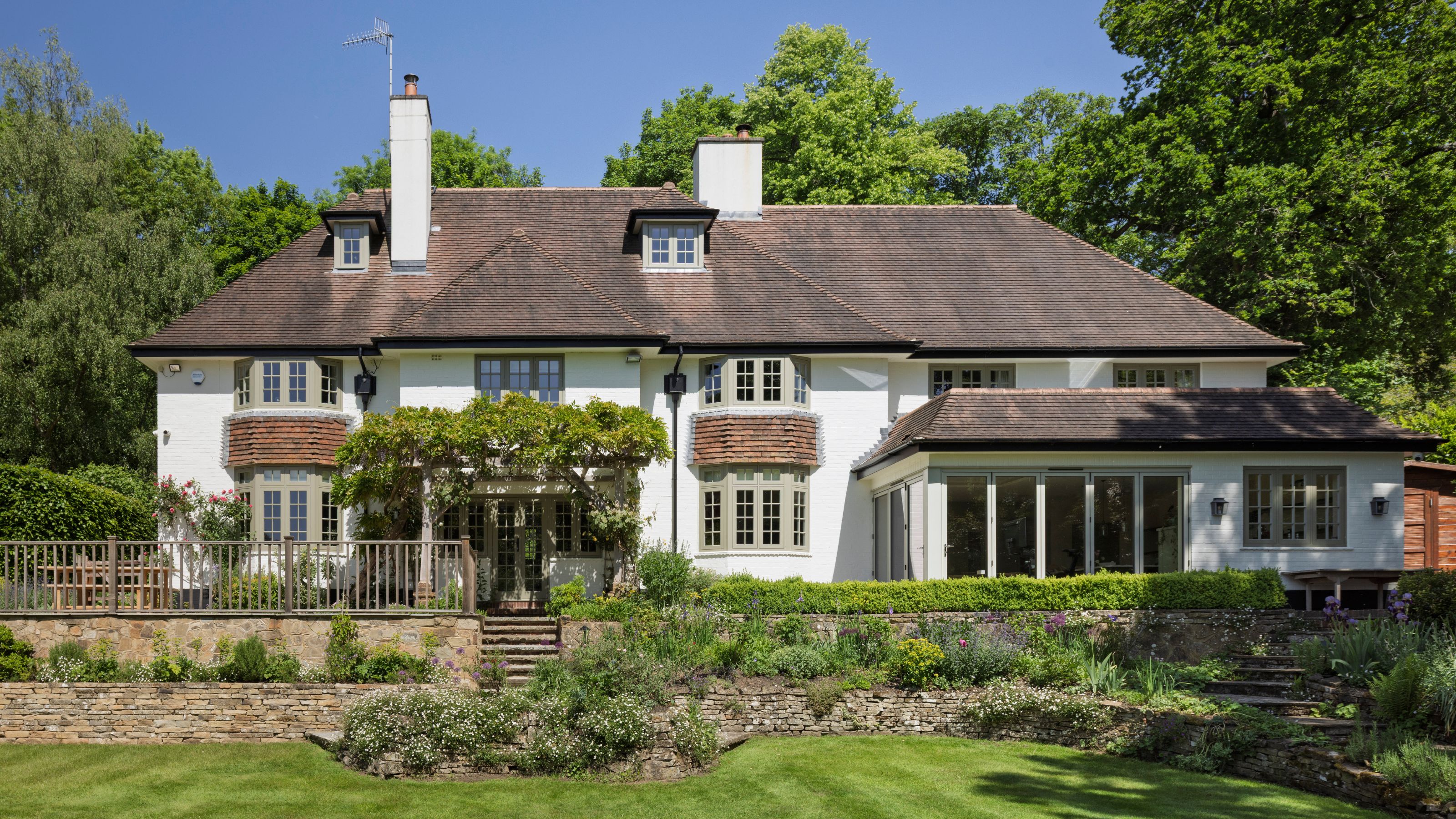 Eine Außenaufnahme eines großen englischen Hauses in Surrey mit einem von Bäumen umgebenen, gestuften Garten