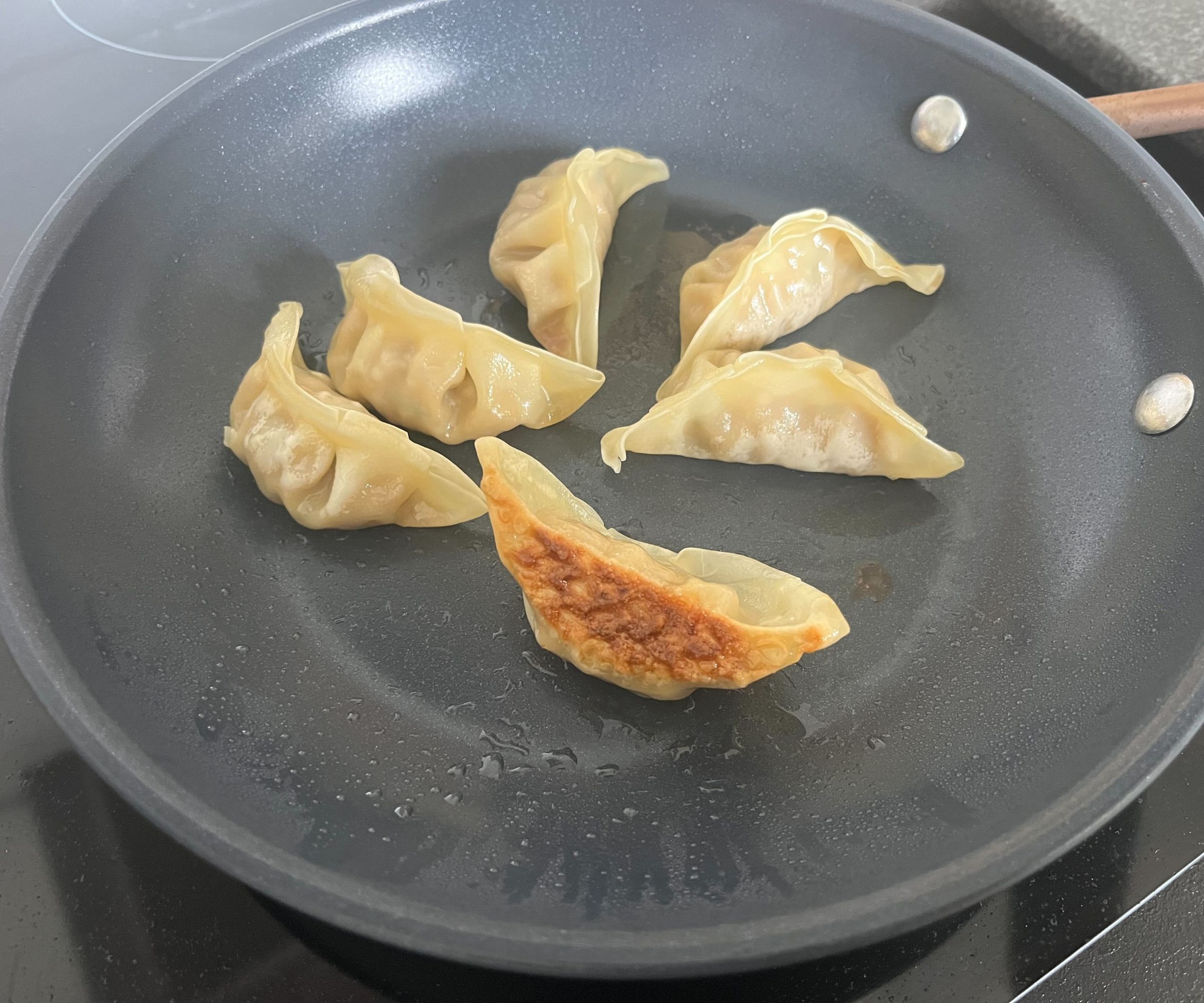 Gyoza wird in einer kleinen blauen Keramikpfanne gebraten, eine auf der Seite, um den goldenen, knusprigen Boden zu zeigen