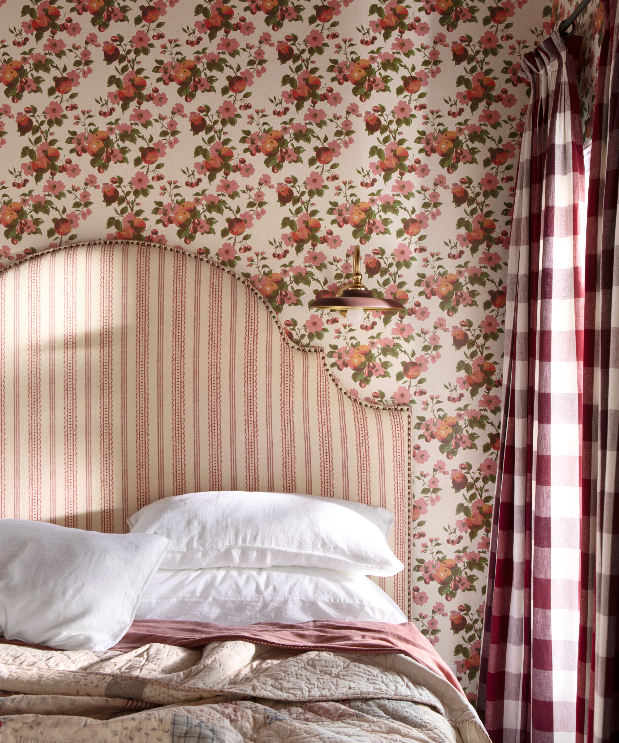 ein Schlafzimmer mit roter Blumentapete, Gingham-Vorhängen und einem gestreiften roten Kopfteil