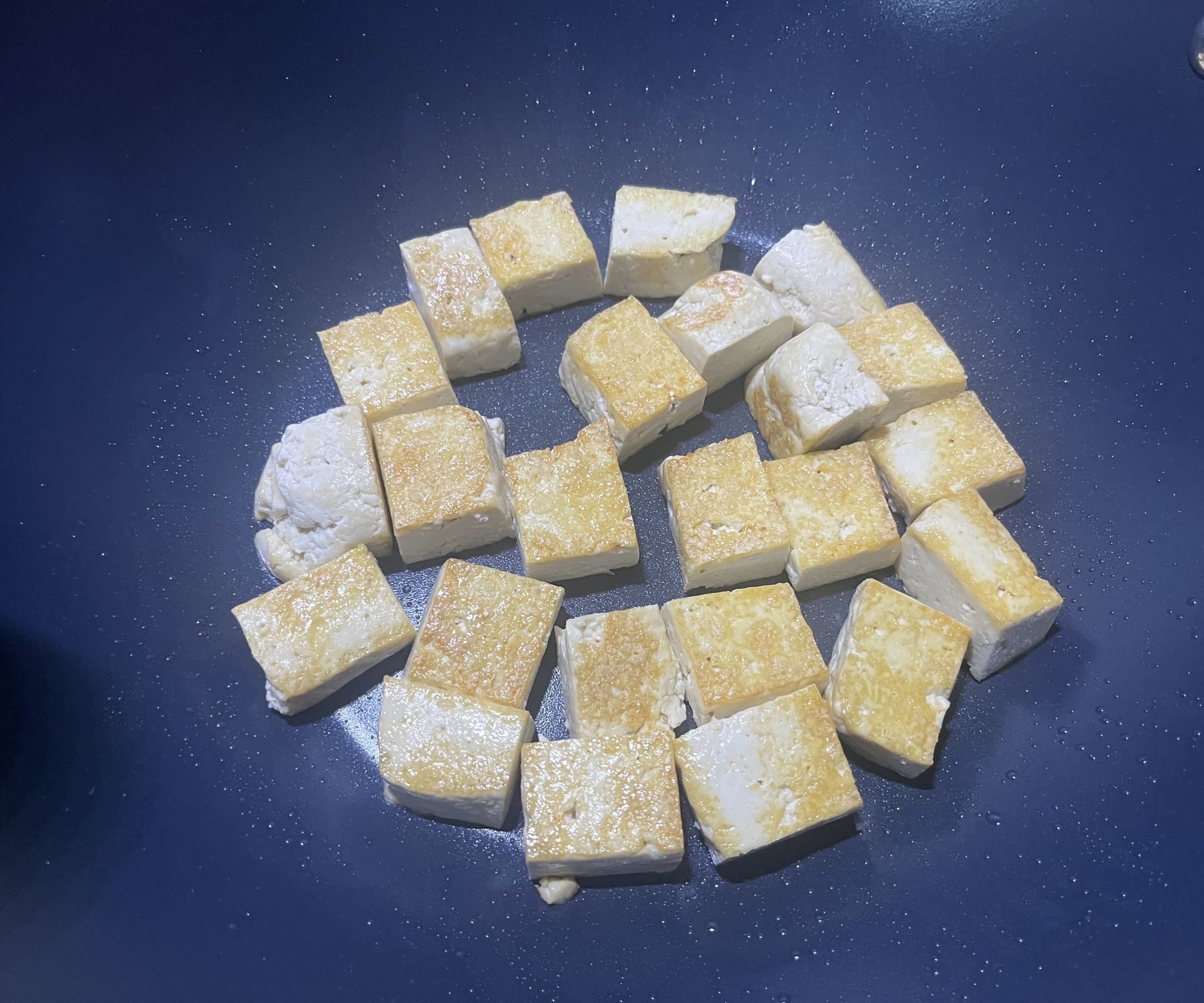 Würfel aus goldgebratenem Tofu auf dem Boden einer blauen Keramikpfanne