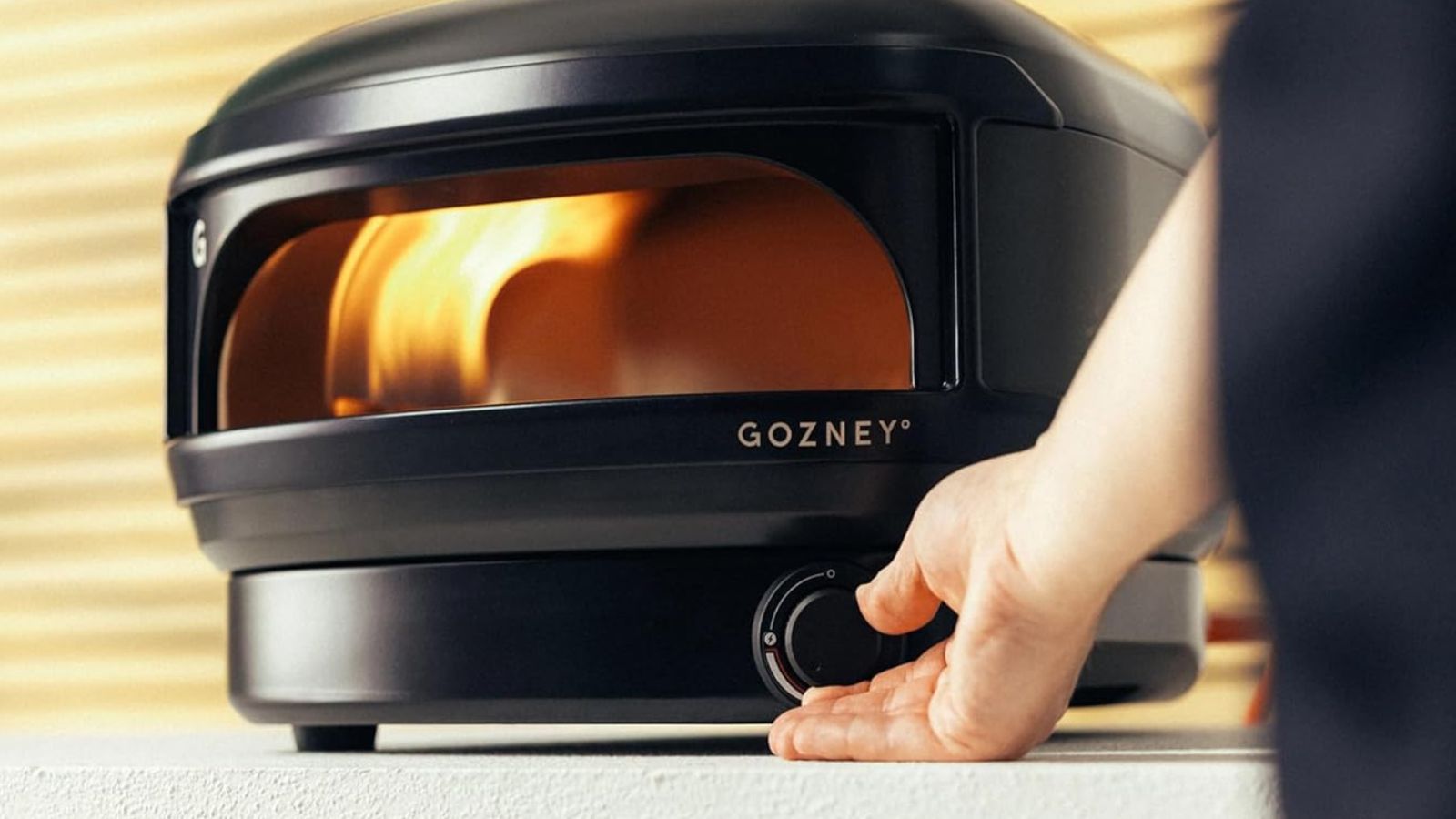 Der schwarze gasbetriebene Pizzaofen Gozney Arc Lite wird von der Hand eines Mannes aufgedreht. 