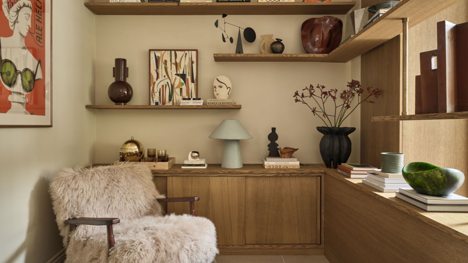 Leseecke mit Holzregalen, dekoriert mit Vasen und Kunstwerken, einem flauschigen Sessel und einem großen roten Druck an der Wand
