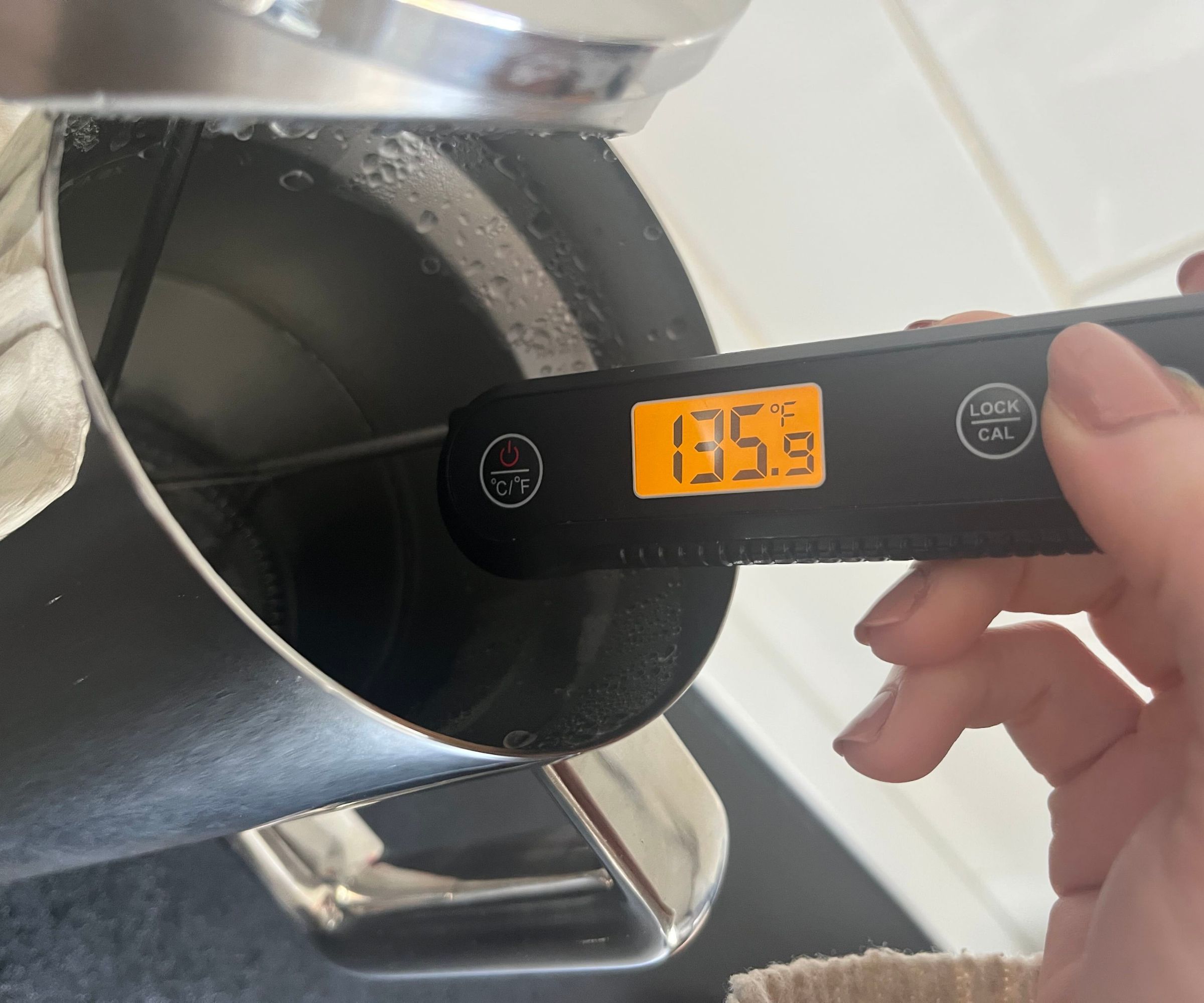 Ein digitales Thermometer, das die Wassertemperatur in einer Kaffeepresse aus Edelstahl misst. Es zeigt 135F