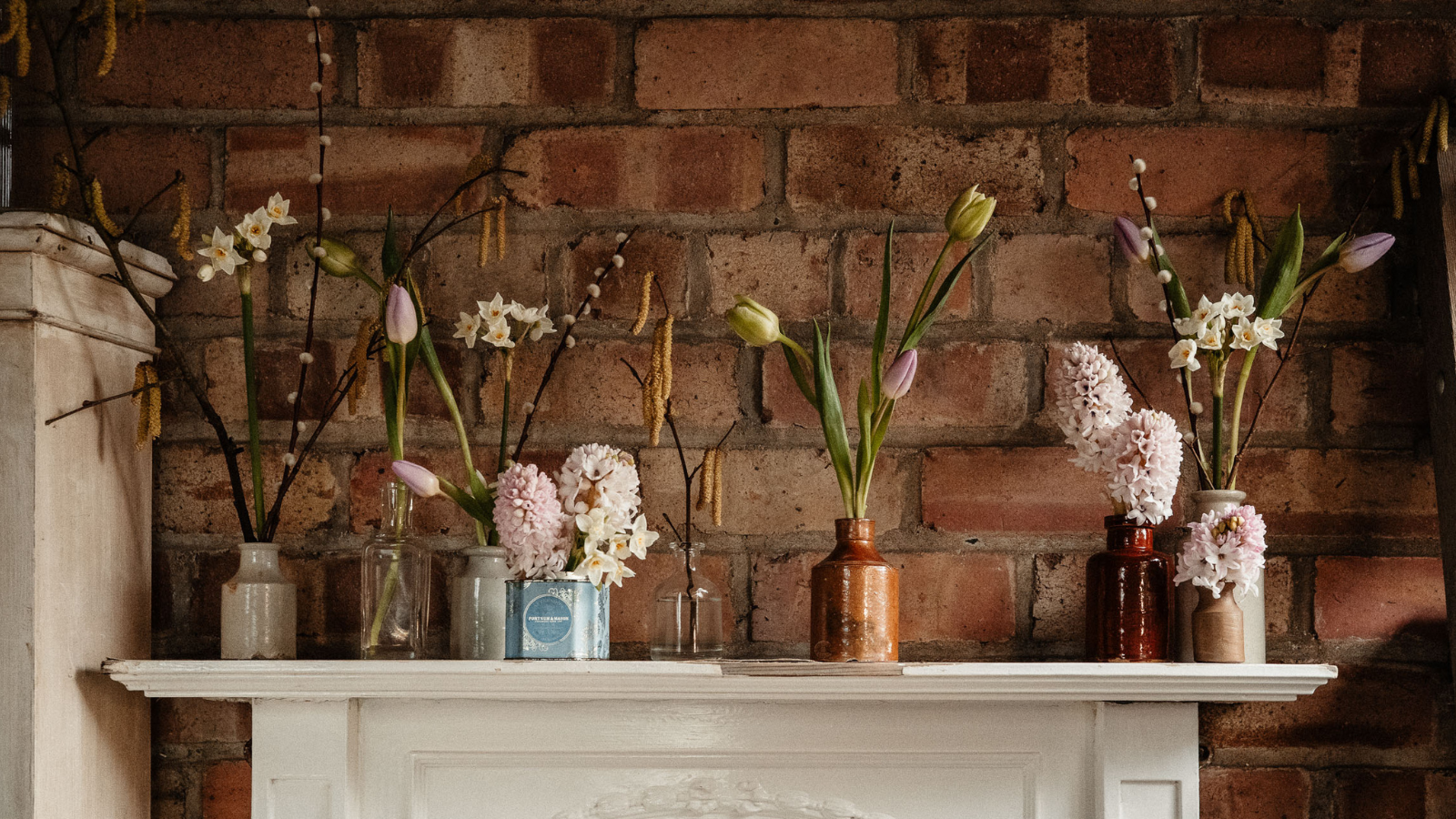 Blumenmuster in Vintage-Gefäßen und keramischen Tintenfässern auf dem Kaminsims vor dem Hintergrund einer roten Backsteinmauer