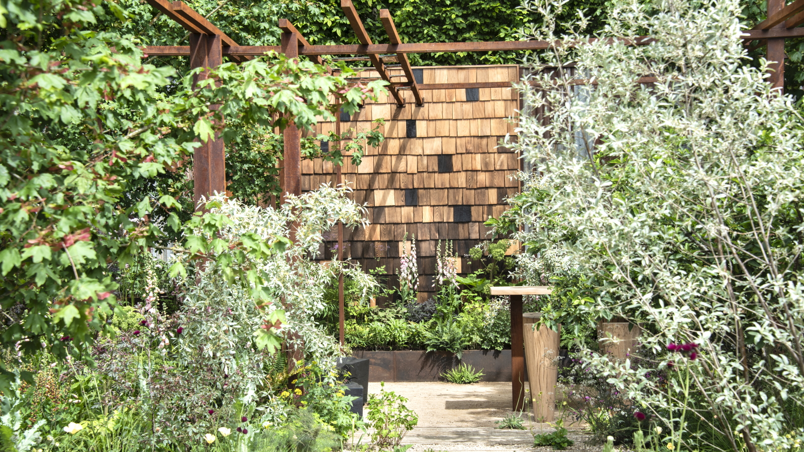 Sträucher und Bäume vor einer Holz- und Metallkulisse auf der RHS Chelsea Flower Show 2026