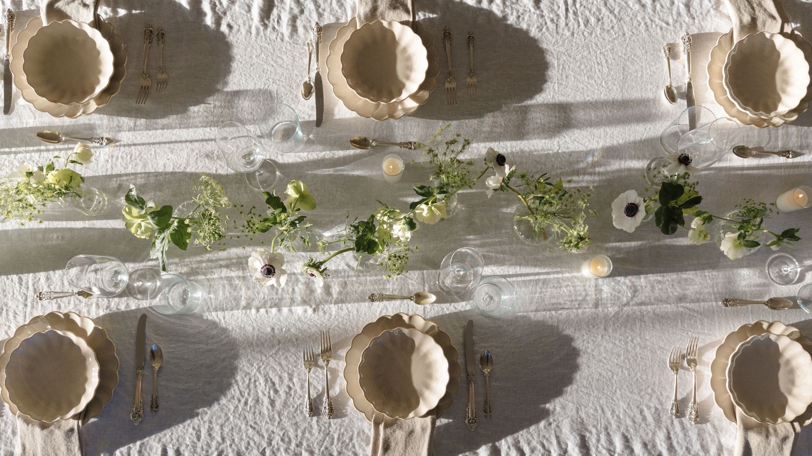 Outdoor tablescape with white linen tablescape, cream scalloped plates and bowls, a floral garland in the centre, and lit candles
