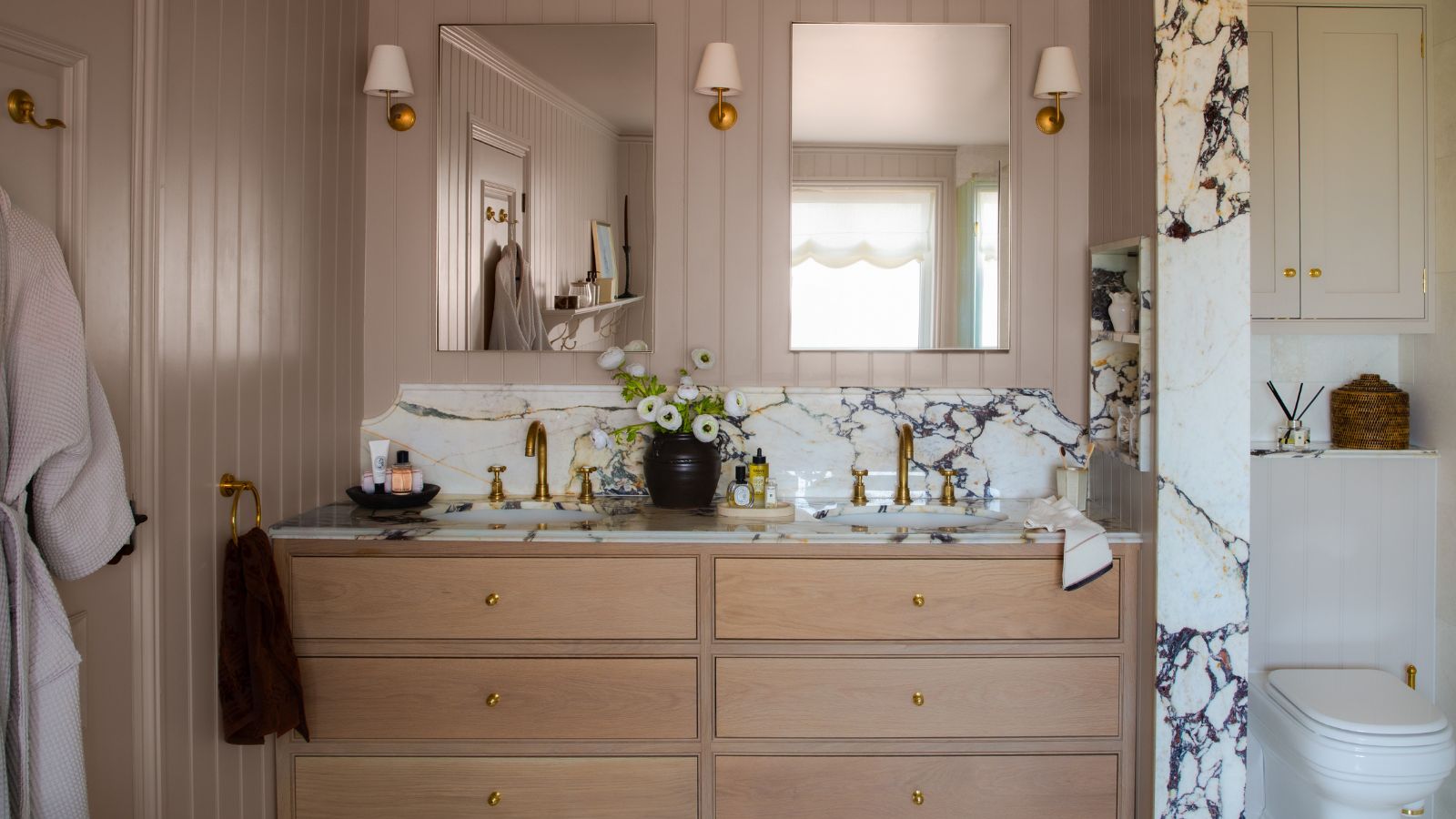 Badezimmer mit Elephant's Breath von Farrow & Kugelbemalte Wände, ein Doppelwaschbecken-Waschtisch mit Marmorarbeitsplatten, Holzschubladen, zwei Spiegel und Wandleuchten auf beiden Seiten.