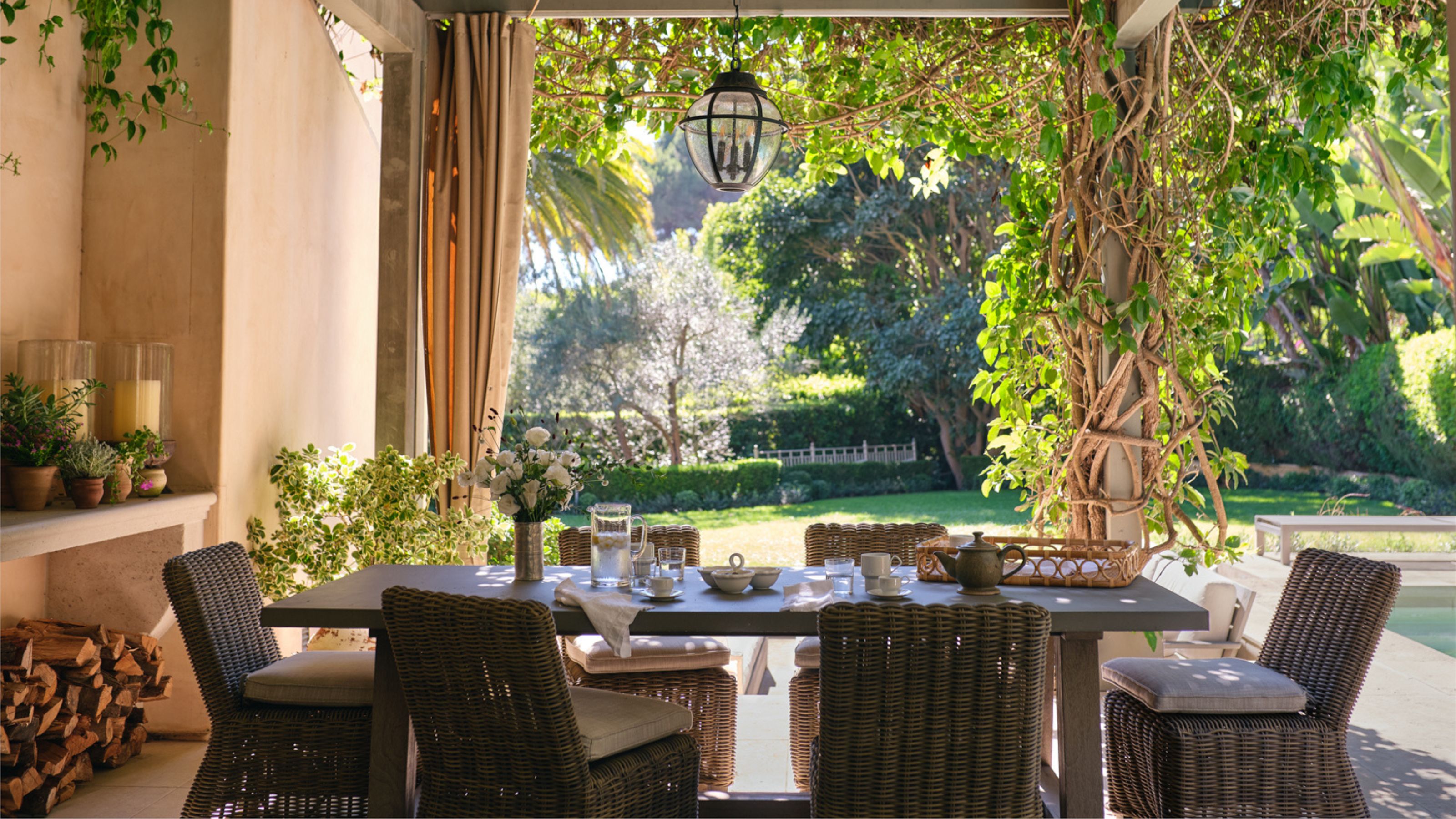 ein mit einer Pergola überdachter Essbereich im Freien mit Rattanstühlen und einem gedeckten Tisch zum Frühstück