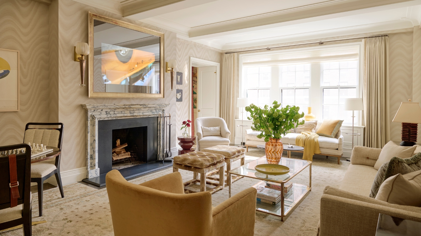 Helles Wohnzimmer mit beige- und cremefarbener Einrichtung, an der Wand montiertem Fernseher, Sofas, Sesseln und einem Fenster, das Tageslicht hereinlässt.