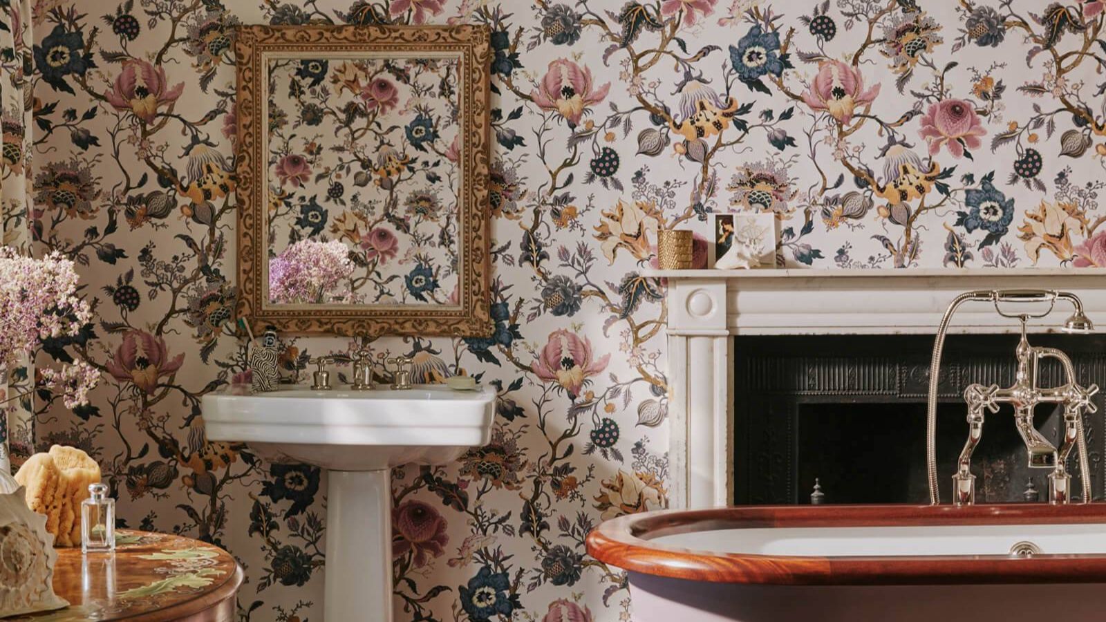 Ein Badezimmer mit Blumenmuster, einem weißen Standwaschbecken und einem verzierten Messingspiegel