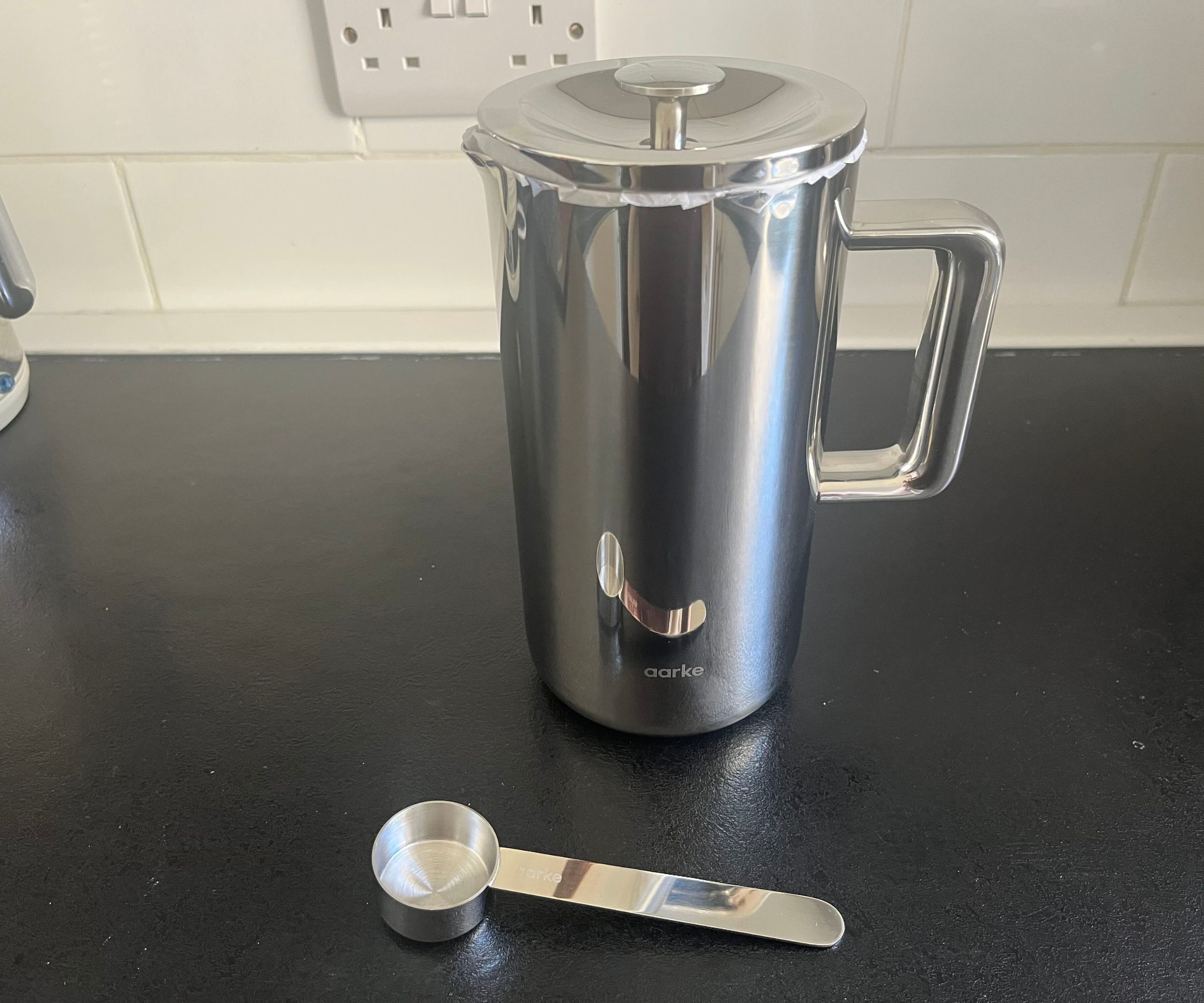 Eine Kaffeepresse aus Edelstahl auf einer schwarzen Theke, mit einem Kaffeelöffel aus Edelstahl