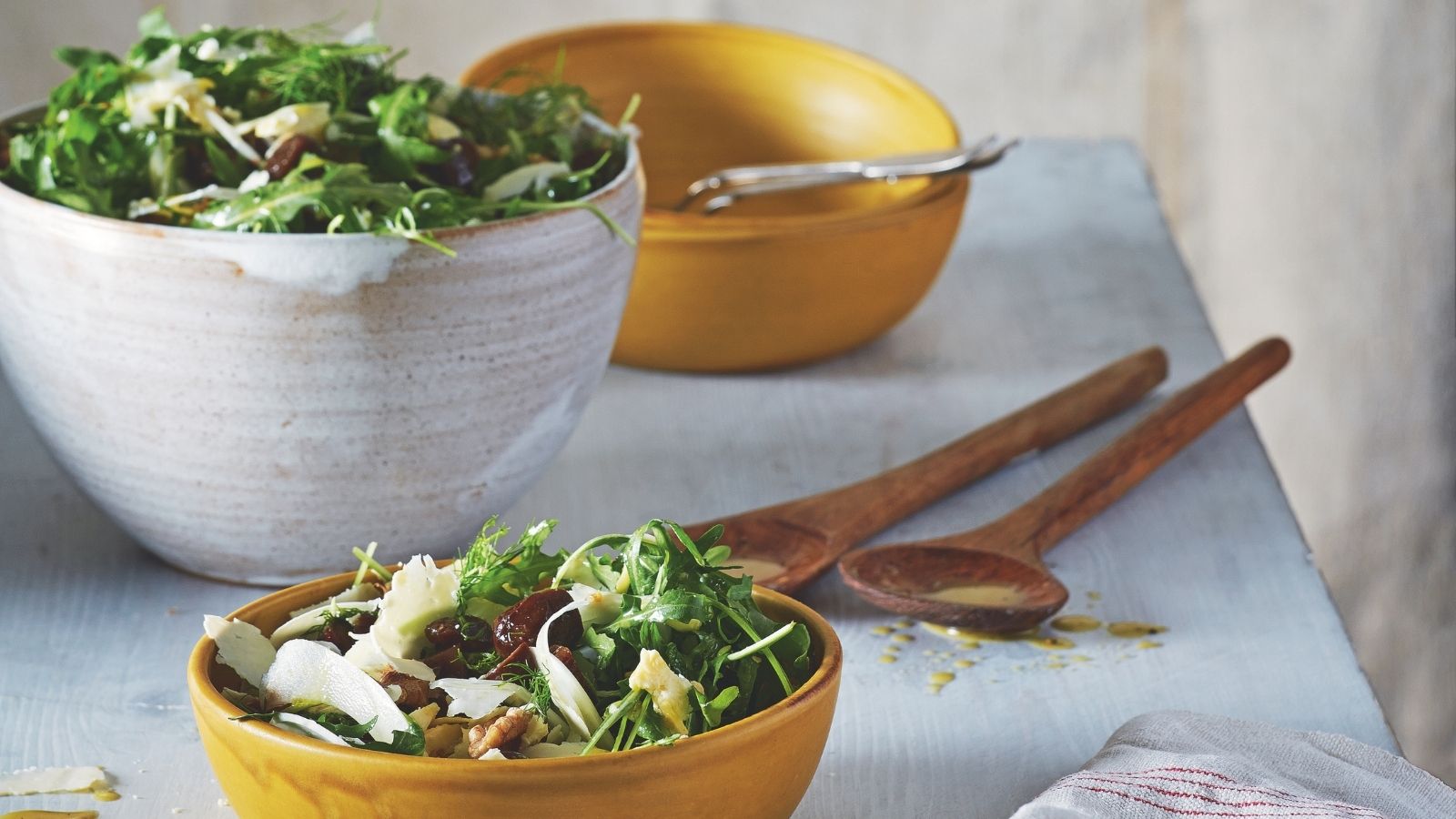 Tisch mit weißen Keramik-Servierschüsseln und gelben Keramikschüsseln mit Salat