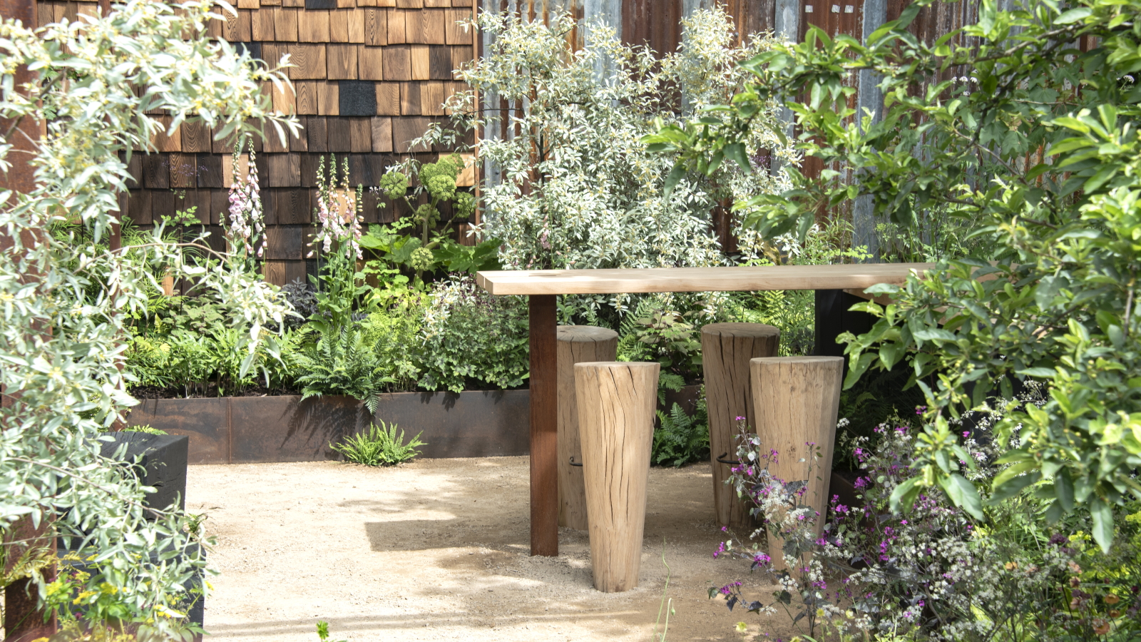 Ein Holztisch und Stühle, umgeben von Hochbeeten mit grünen Sträuchern auf der RHS Chelsea Flower Show 2026